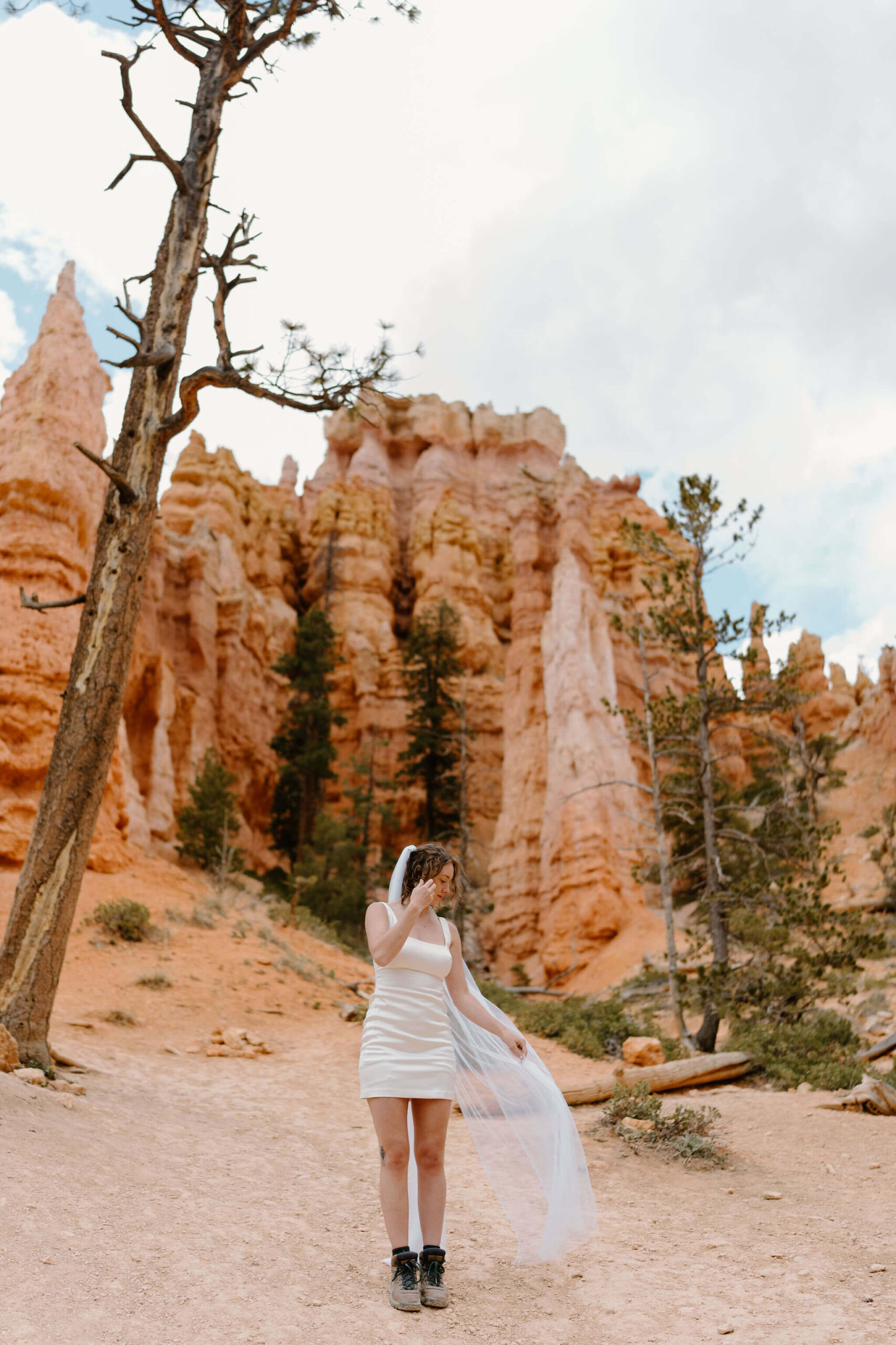bride wearing a short white wedding dress and hiking boots, letting her long veil blow in the breeze at the Queen's Garden viewpoint