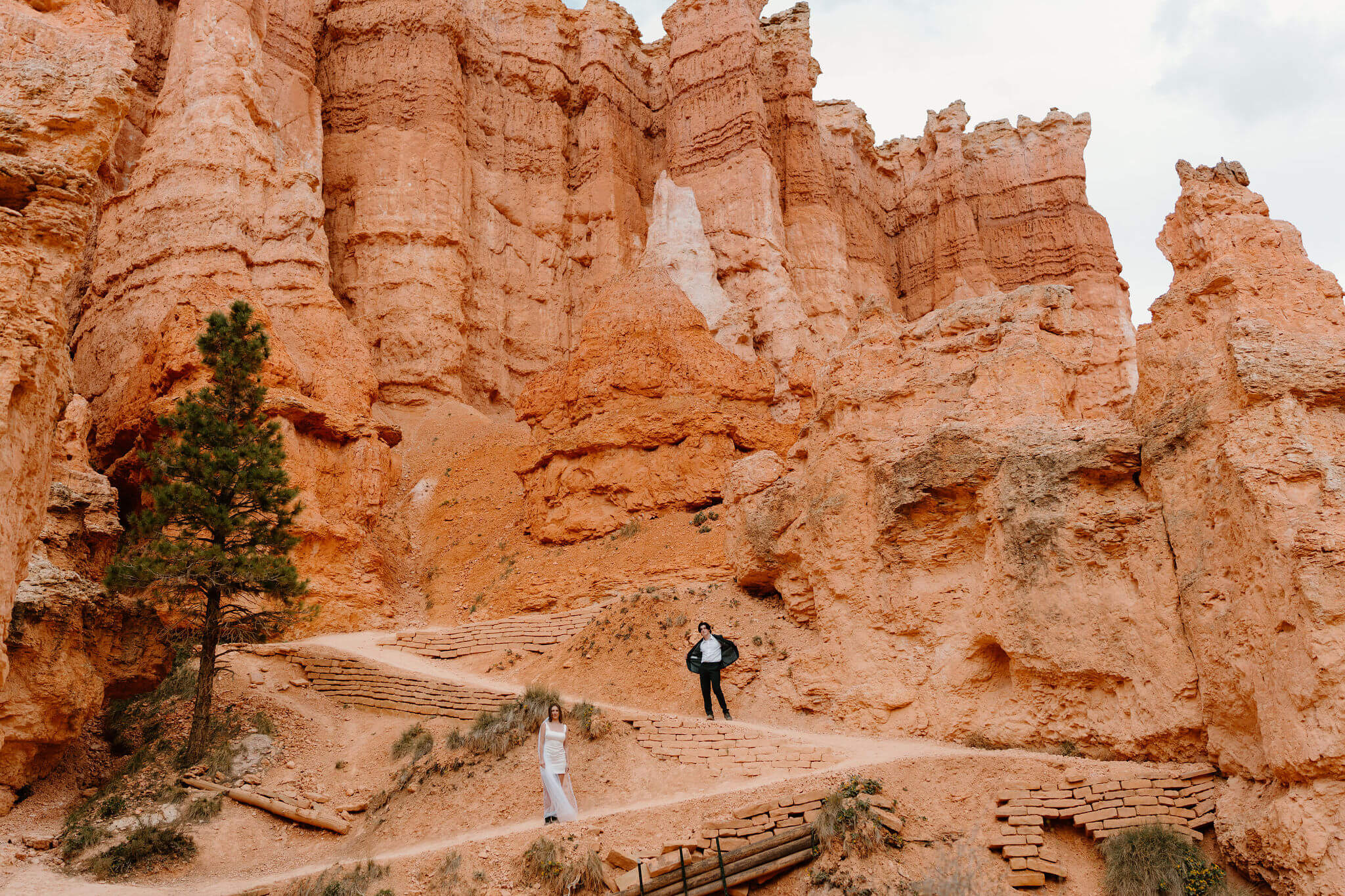 bride and groom striking a silly pose on different levels of a switchback on the Queen's Garden trail at Bryce Canyon National Park