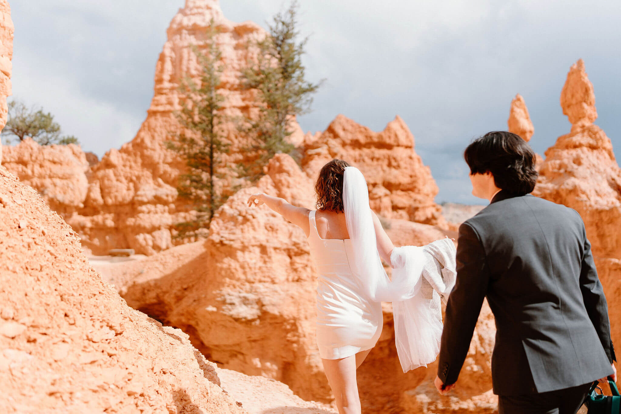 bride and groom walking through tall red rock formations, with dark storm clouds in the distance
