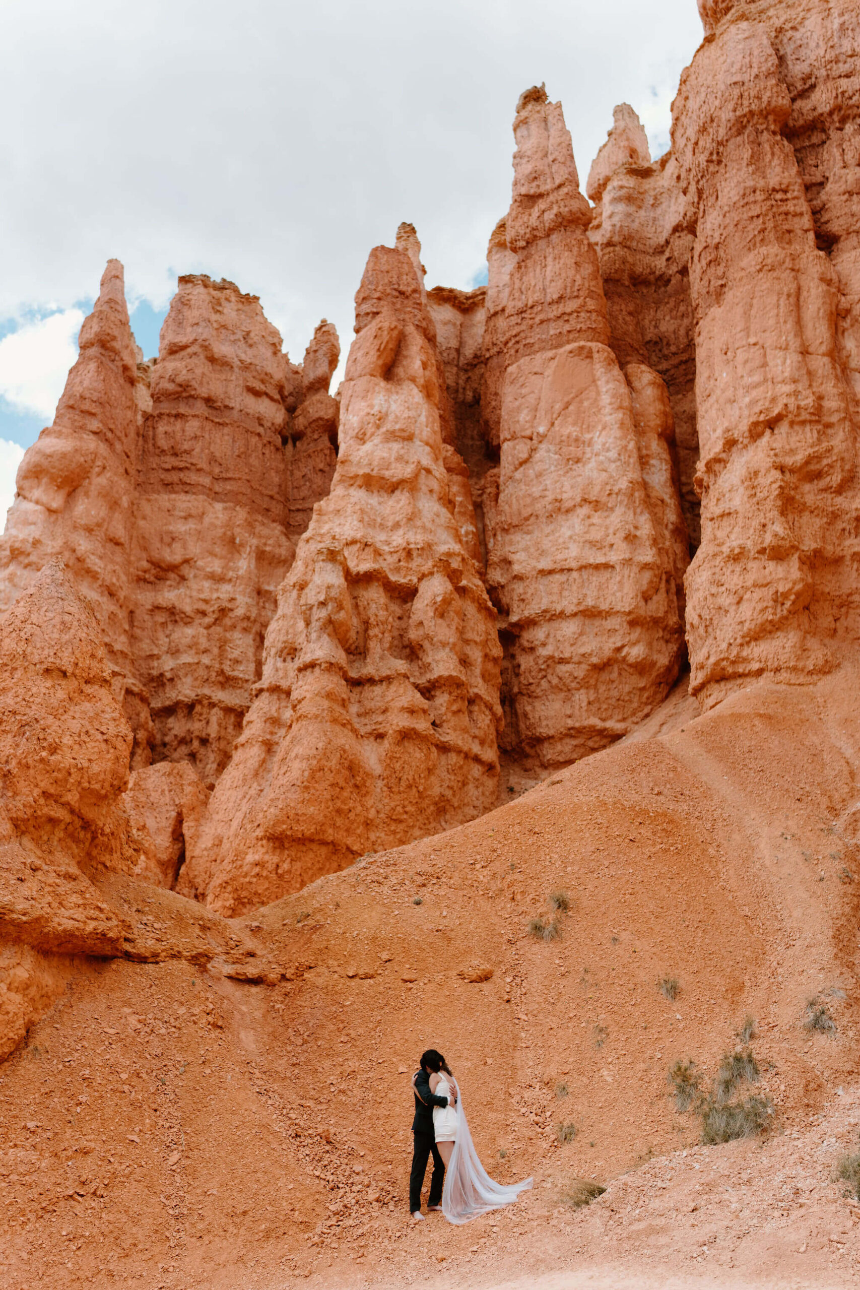 bride and groom embracing with a large wall of red hoodoos behind them