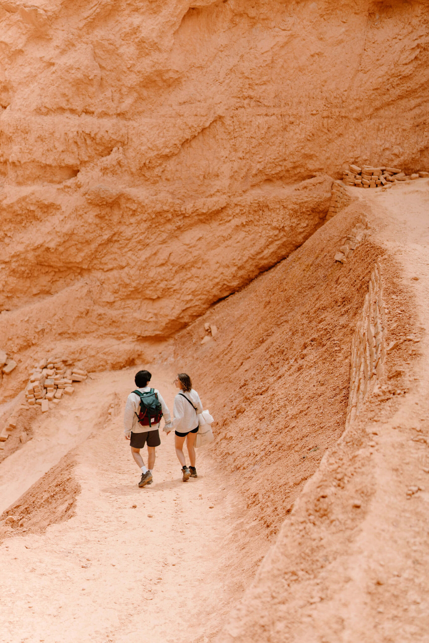 man and woman holding hands and walking away from camera down red-rock switchbacks at Bryce Canyon National Park.