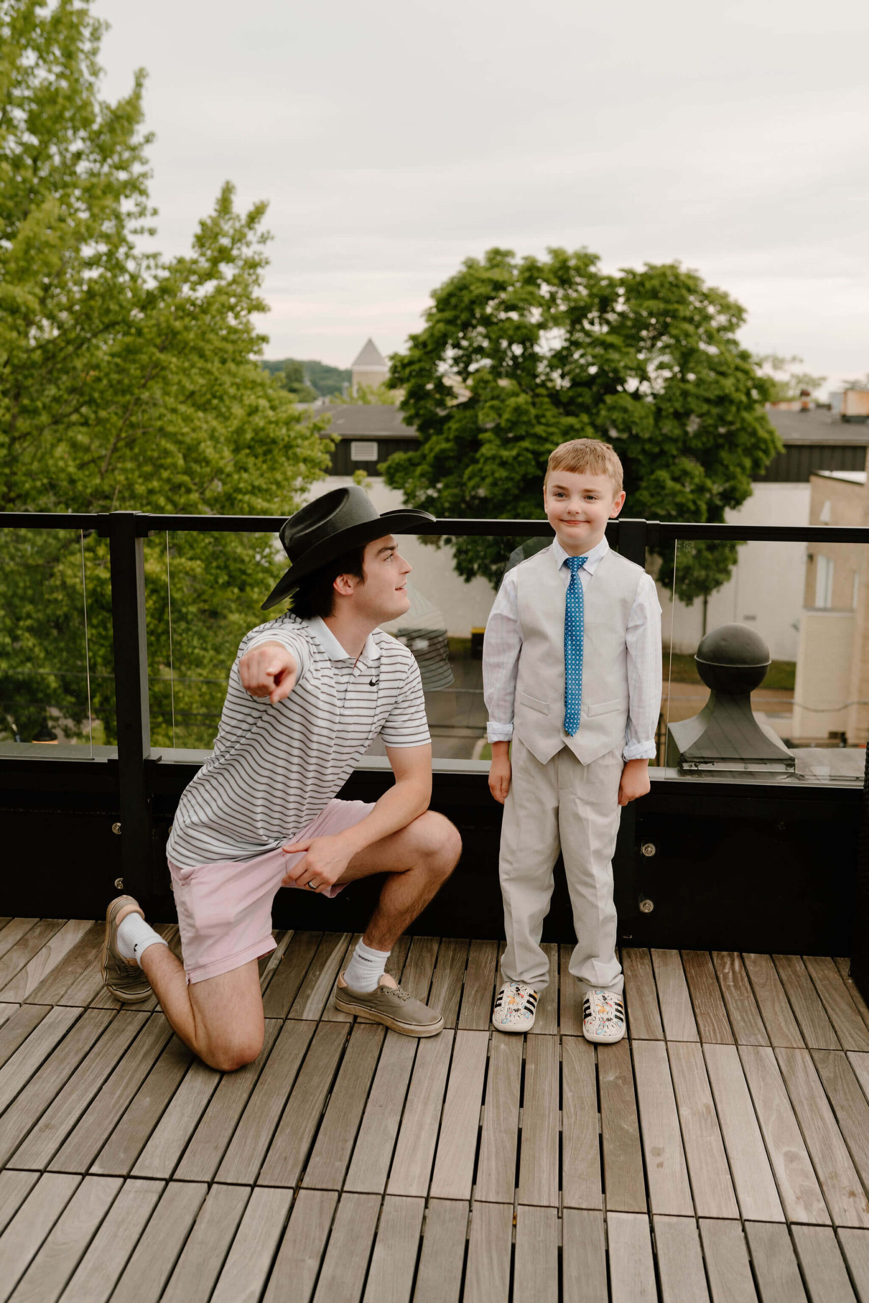 groom kneeling by a young cousin, pointing toward the camera and telling him to smile