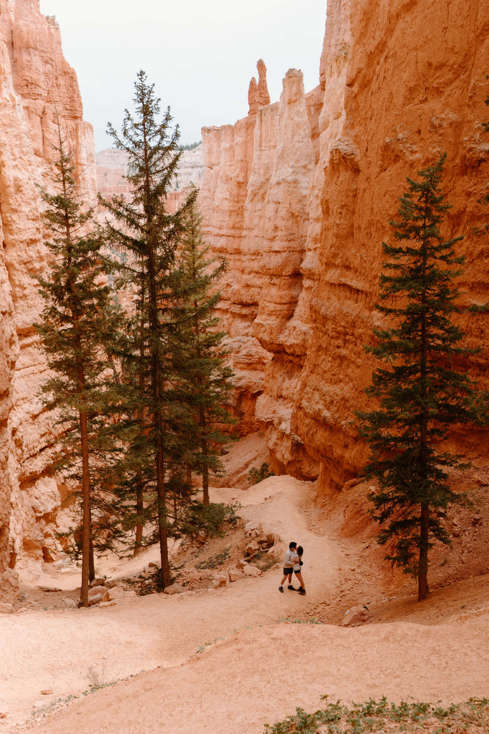 man and woman on a red rock switchback trail through hoodoos