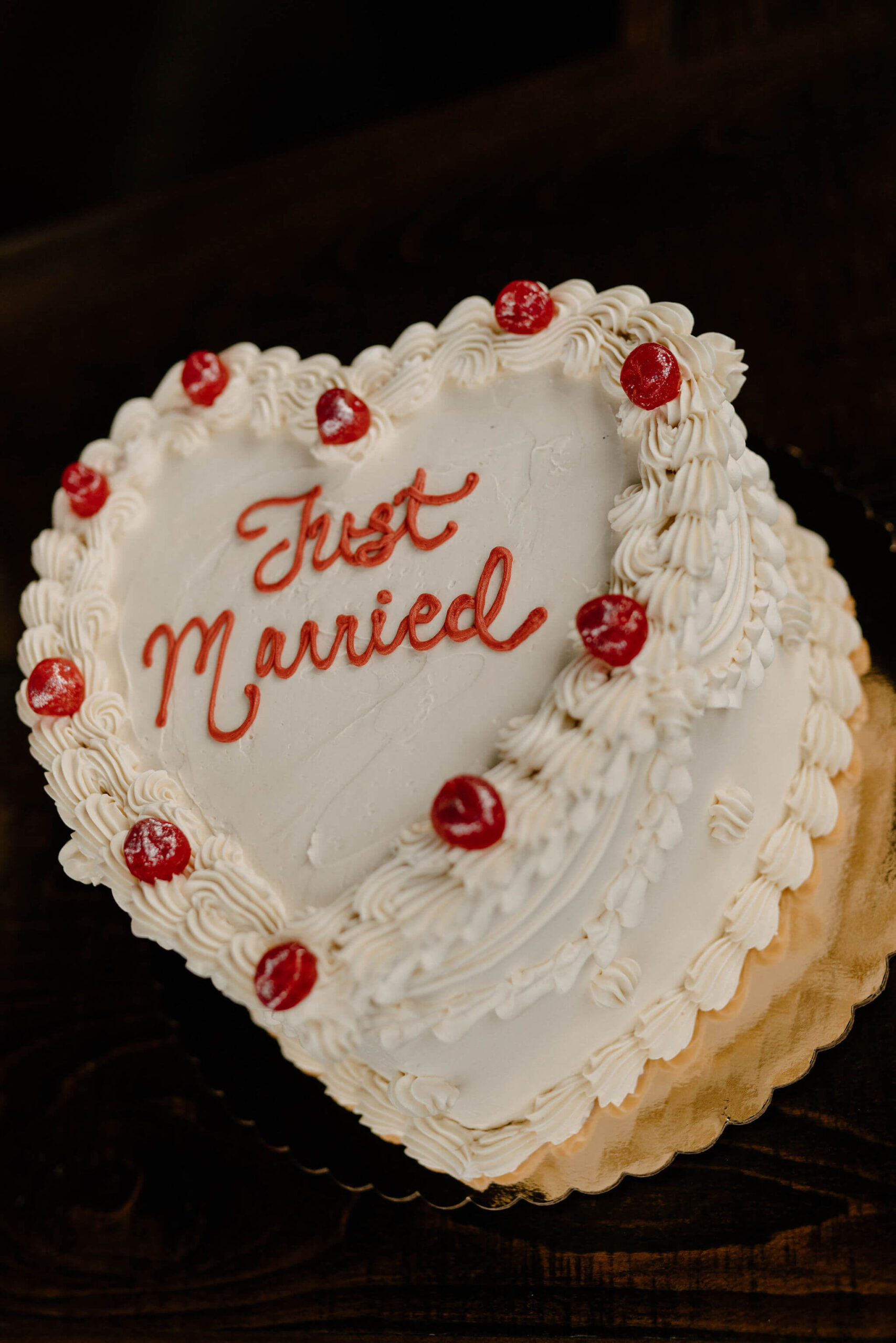 retro-style heart shaped wedding cake with "Just Married" piped in red, with cherries around the ruffled piping