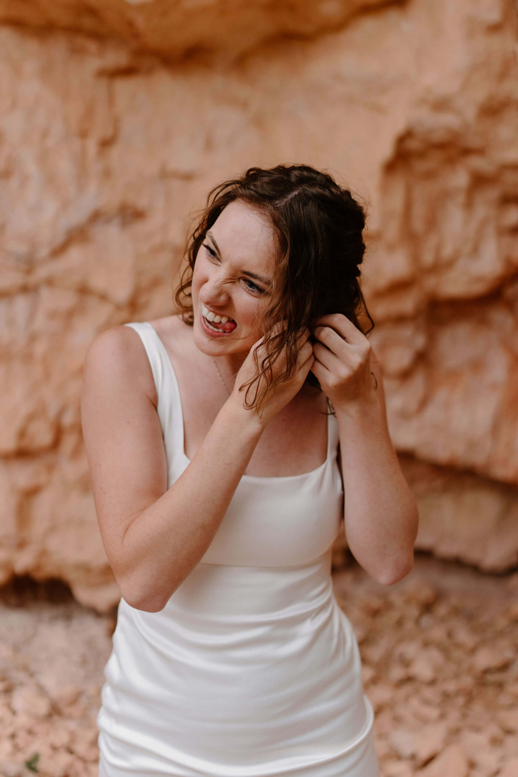 bride in white square neck sleeveless dress putting in earrings against a red rock backdrop
