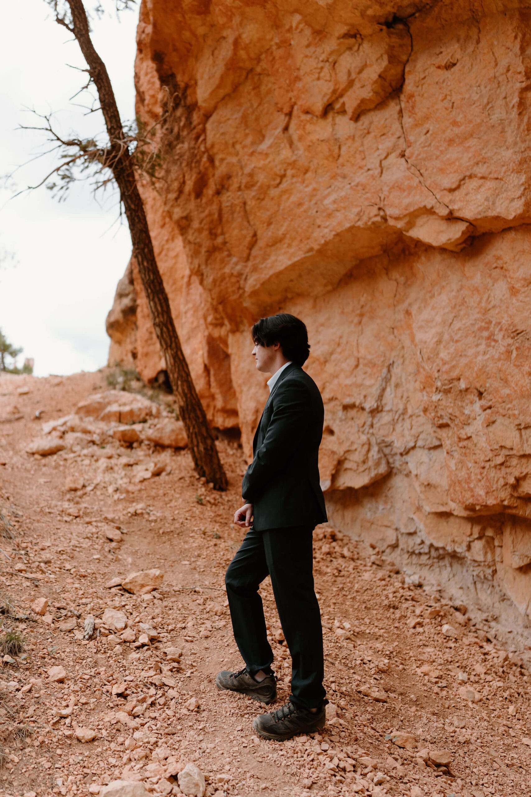 groom in a black suit and hiking boots standing against a red rock background before a first look