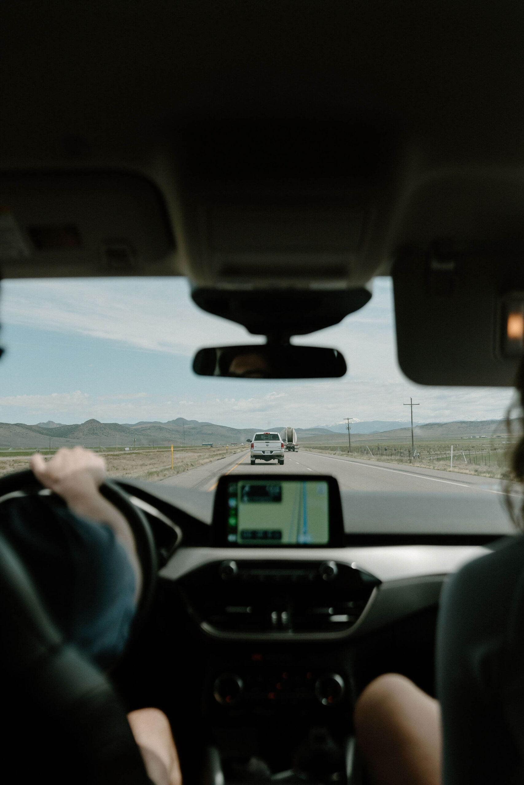 photo from the backseat of the car out the front windshield of a car driving on a highway, the driver's right hand on the wheel