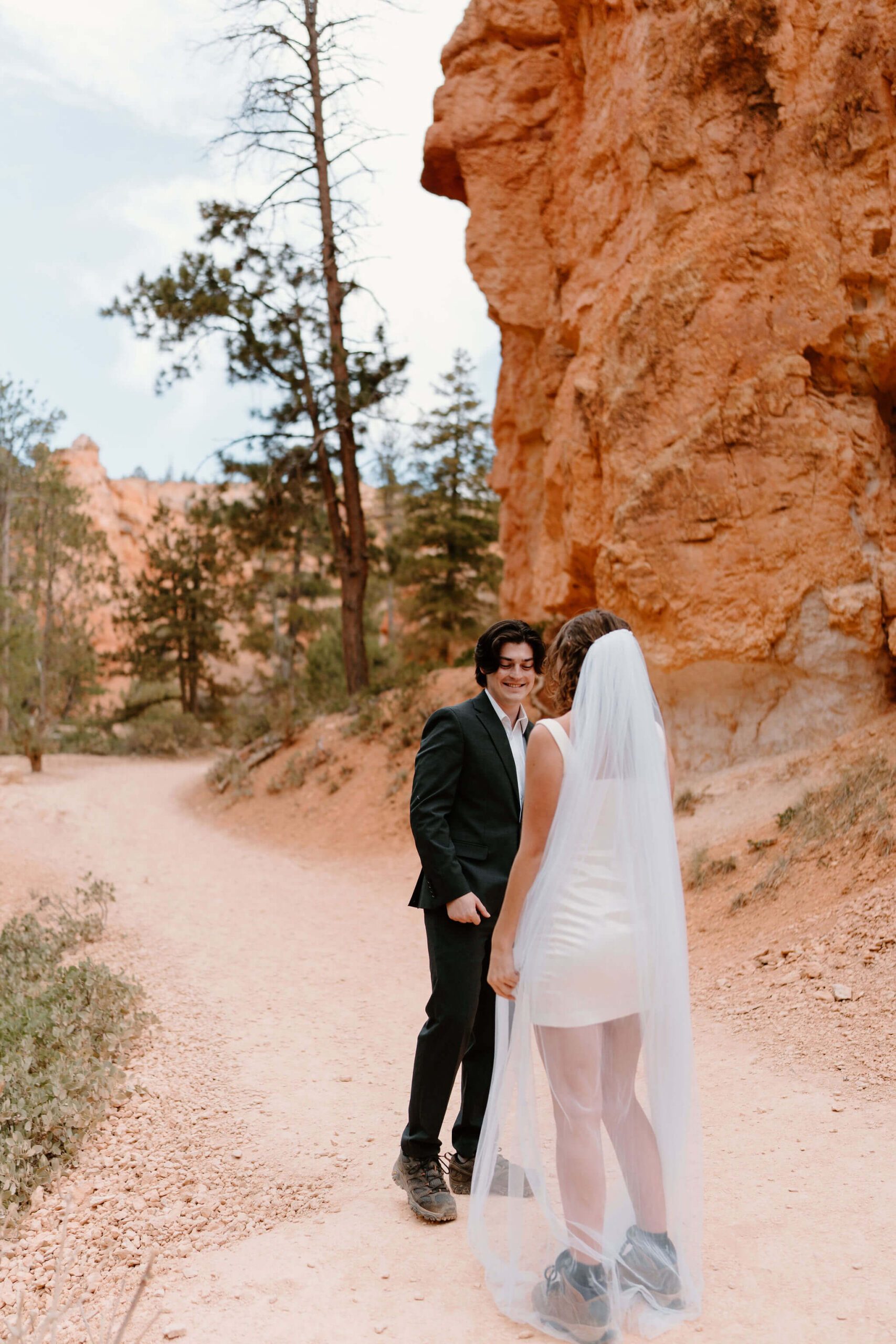 groom (black suit) smiling and seeing bride for the first time during first look on a red rock hiking trail