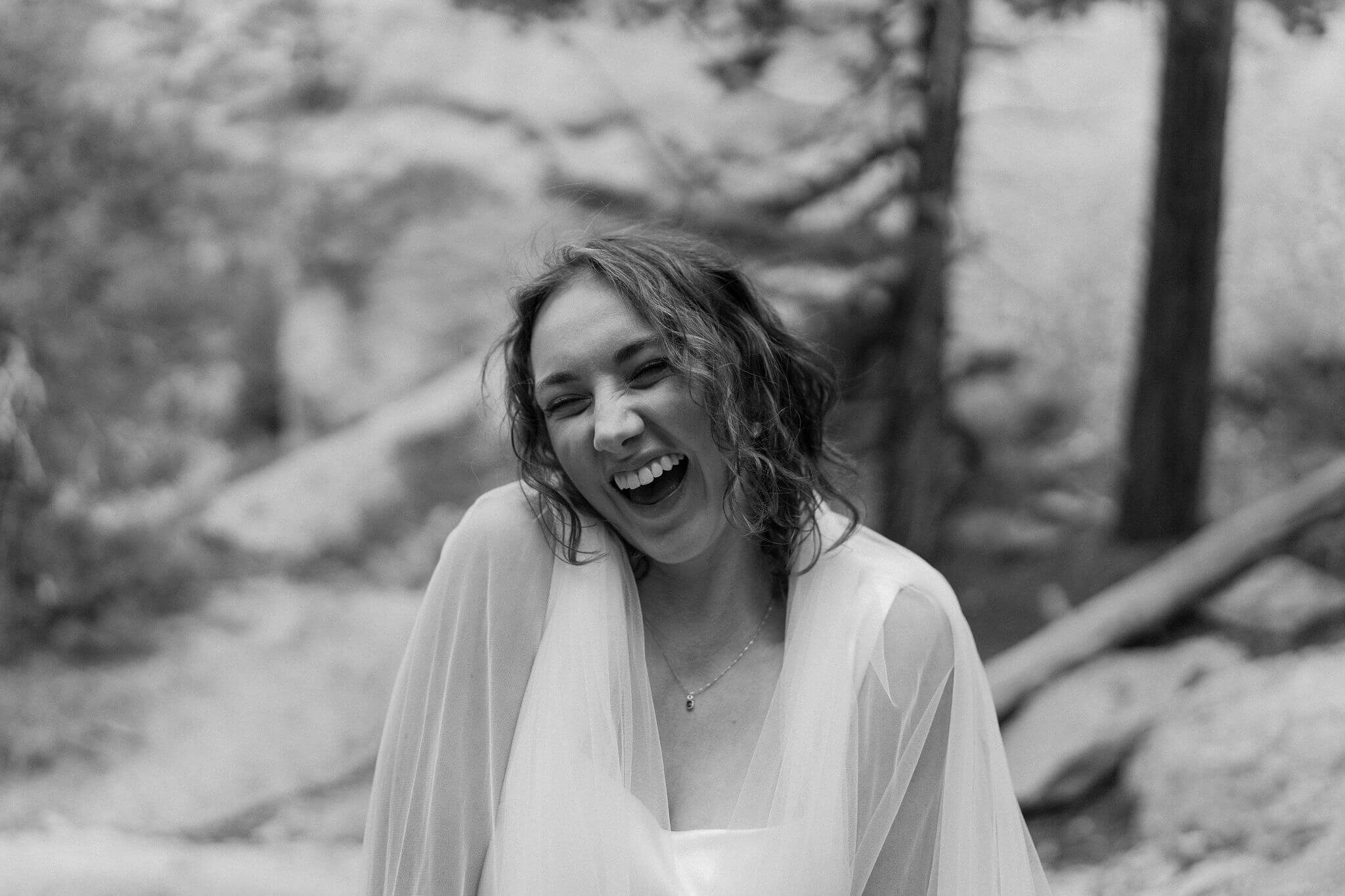 black and white image of bride with veil around her shoulders, smiling widely with her eyes closed