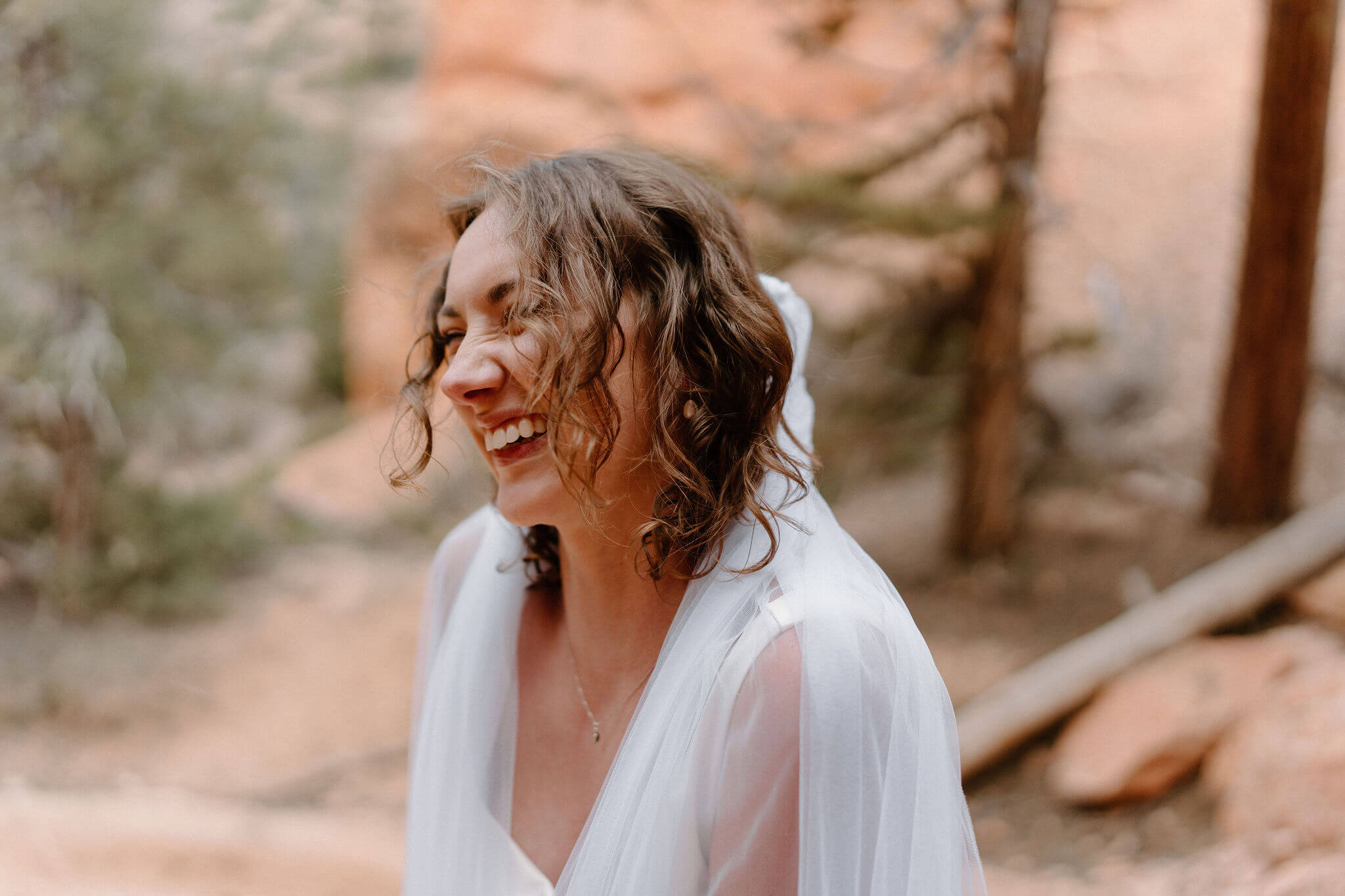 bride with veil around her shoulders, smiling and laughing with her eyes closed
