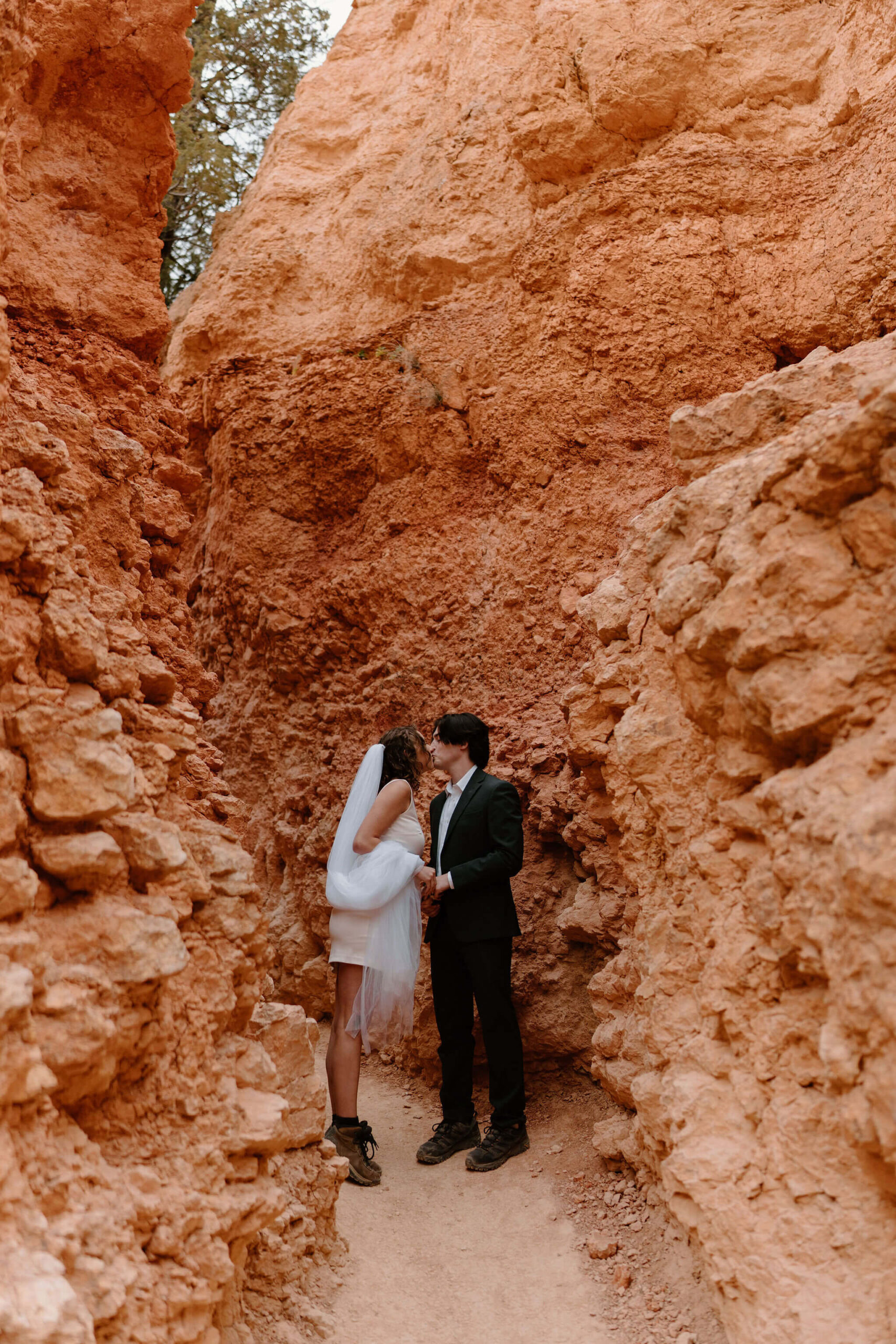 bride and groom kissing on a narrow trail surrounded by tall red rocks in Bryce Canyon National Park