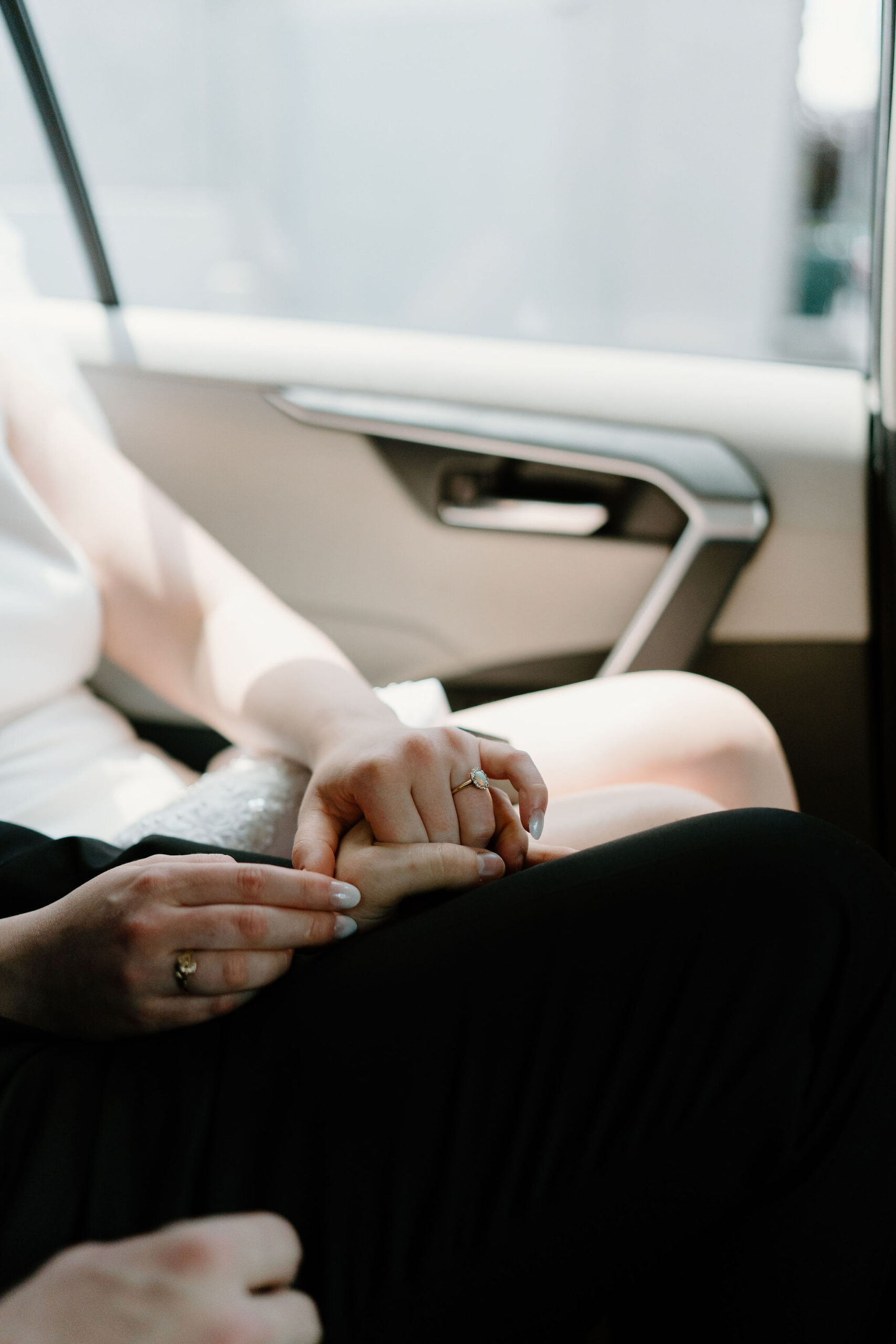 close up of bride and groom holding hands in the back of a car on their elopement day, focused on her wedding ring