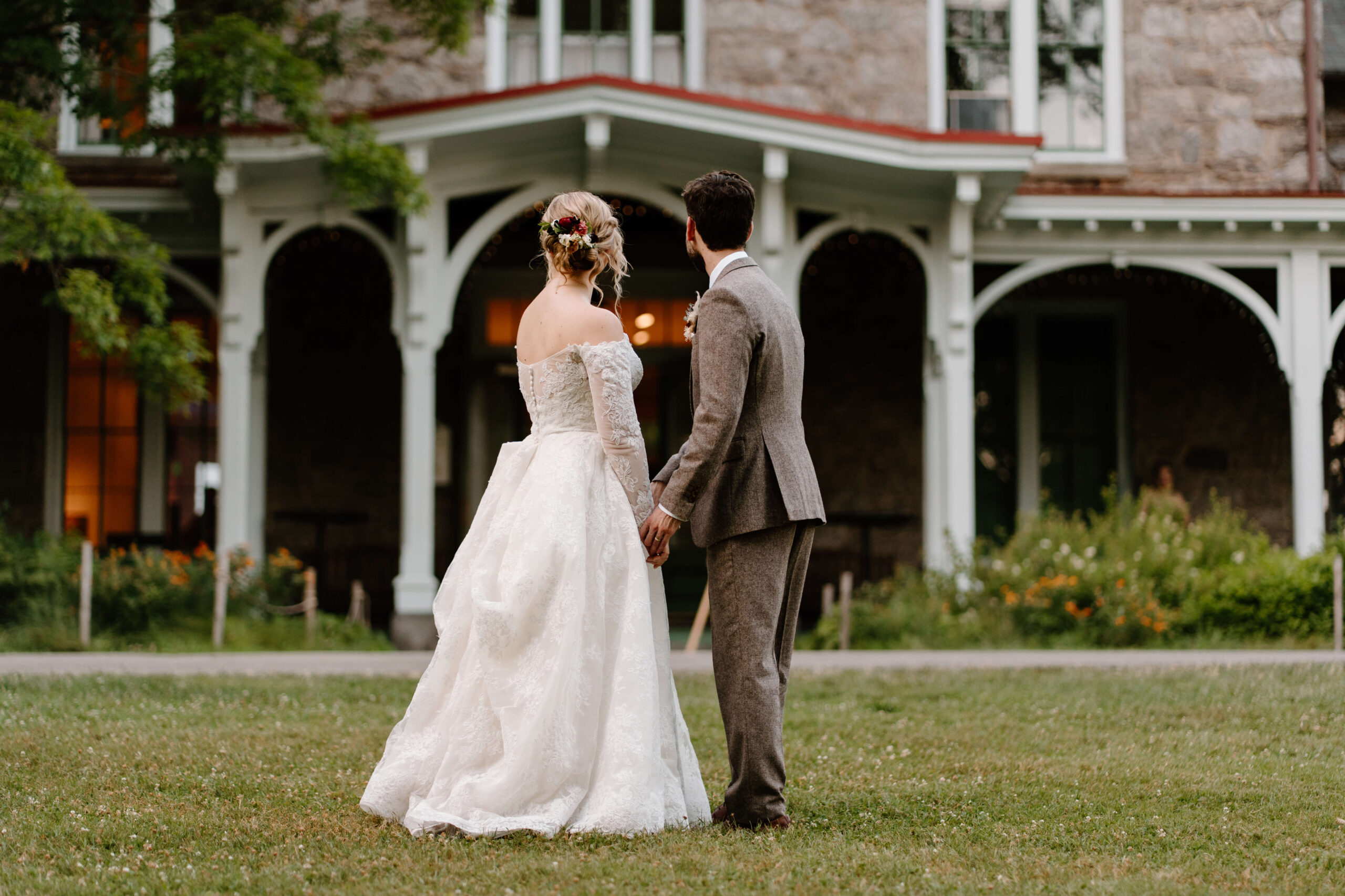 Bride and groom on their wedding day, holding hands in front of the mansion at Morris Arboretum and Gardens and looking toward the home