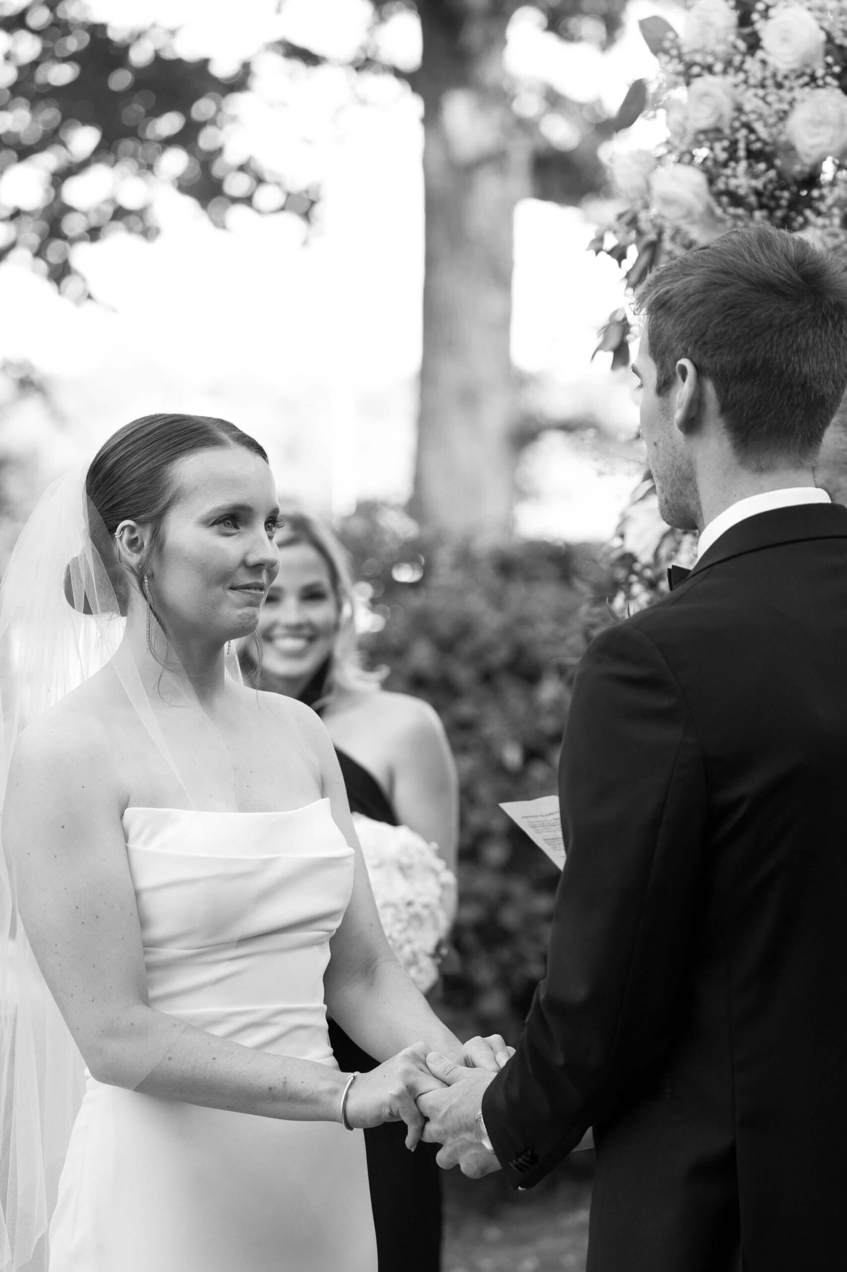 black and white image of a bride and groom holding hands during their wedding ceremony, smiling at each other