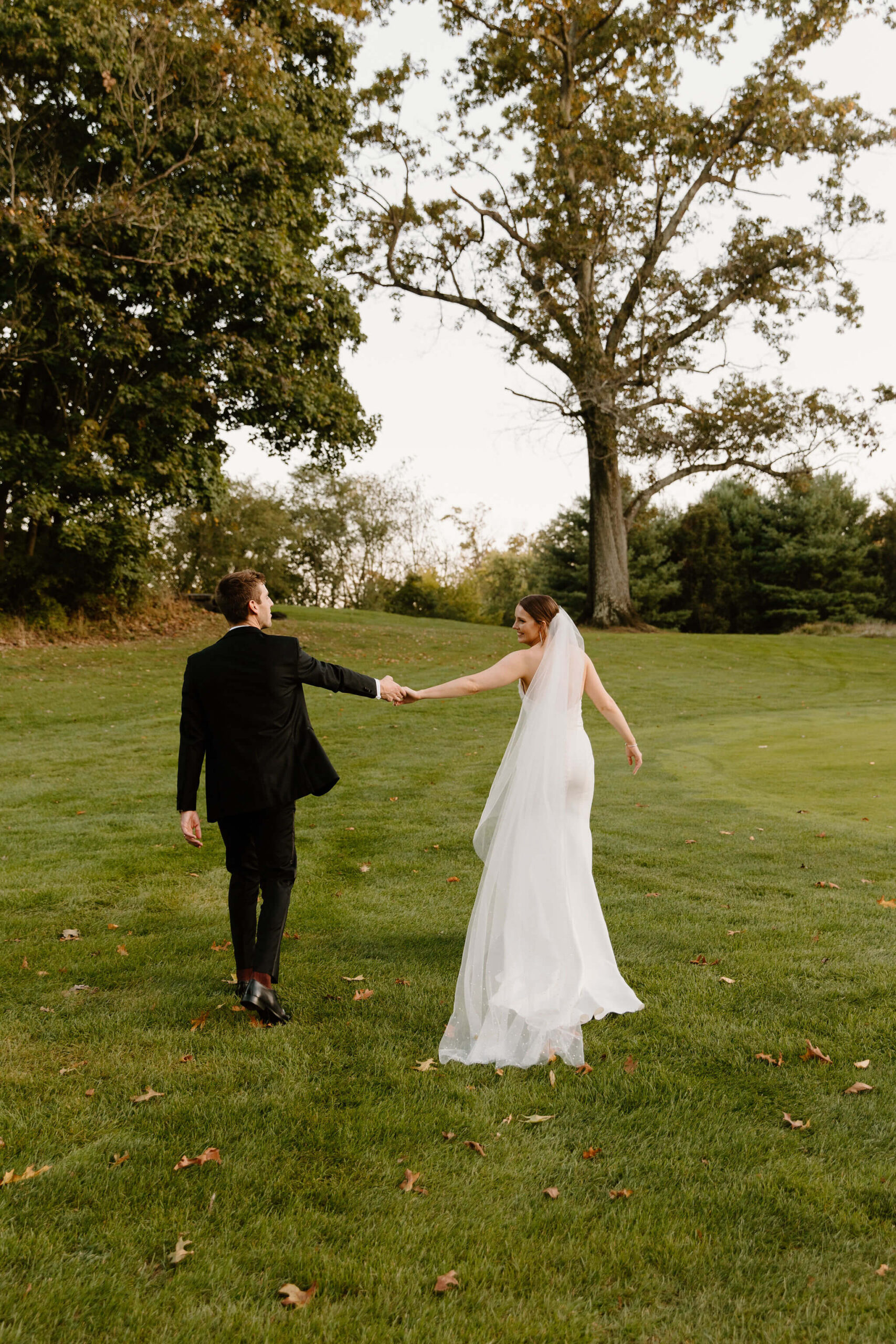 bride and grooms holding hands, far apart from each other, walking away from the camera in a grassy field during golden hour