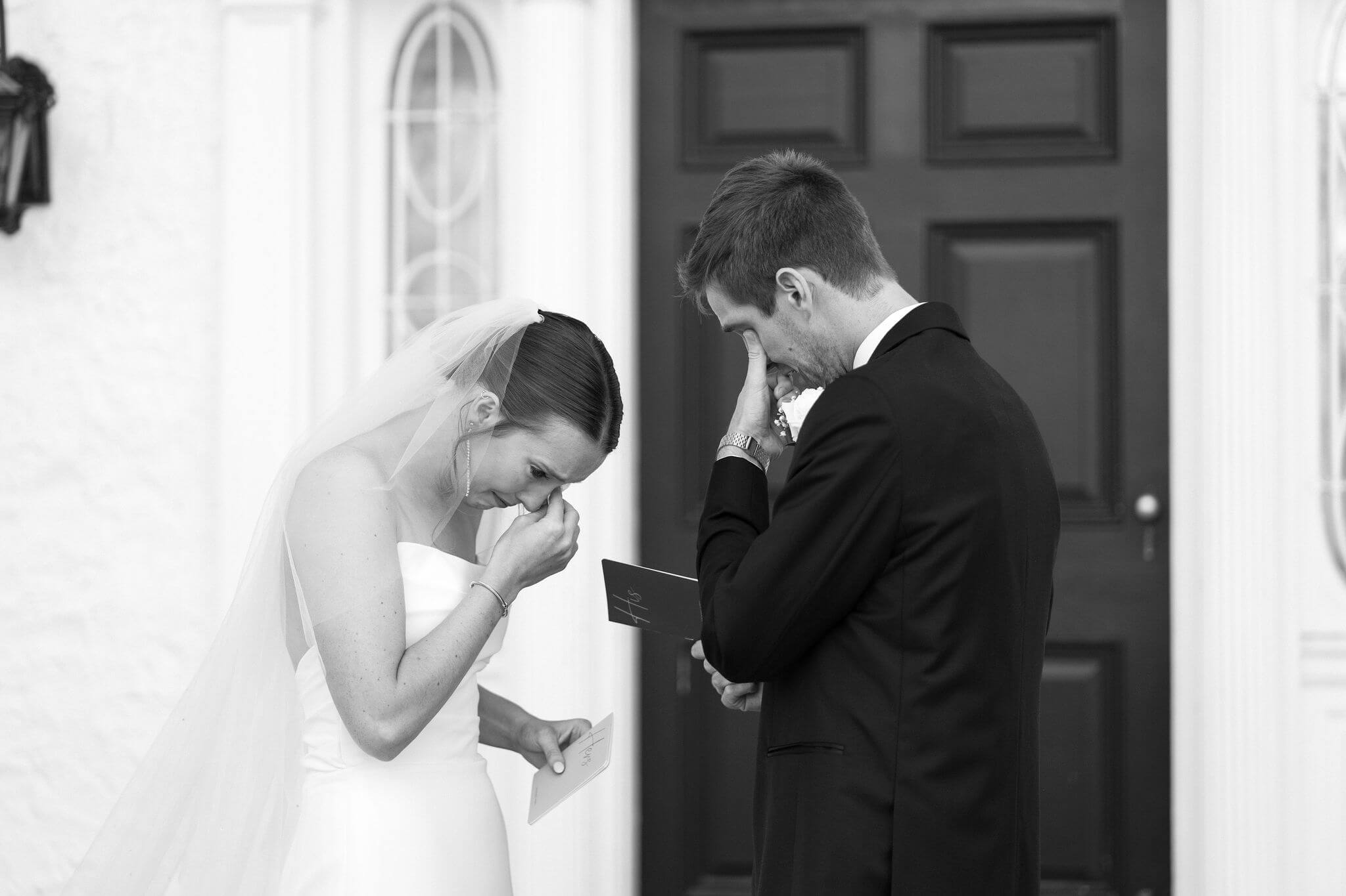 black and white close up image of a bride and groom exchanging wedding vows, both wiping their eyes while crying