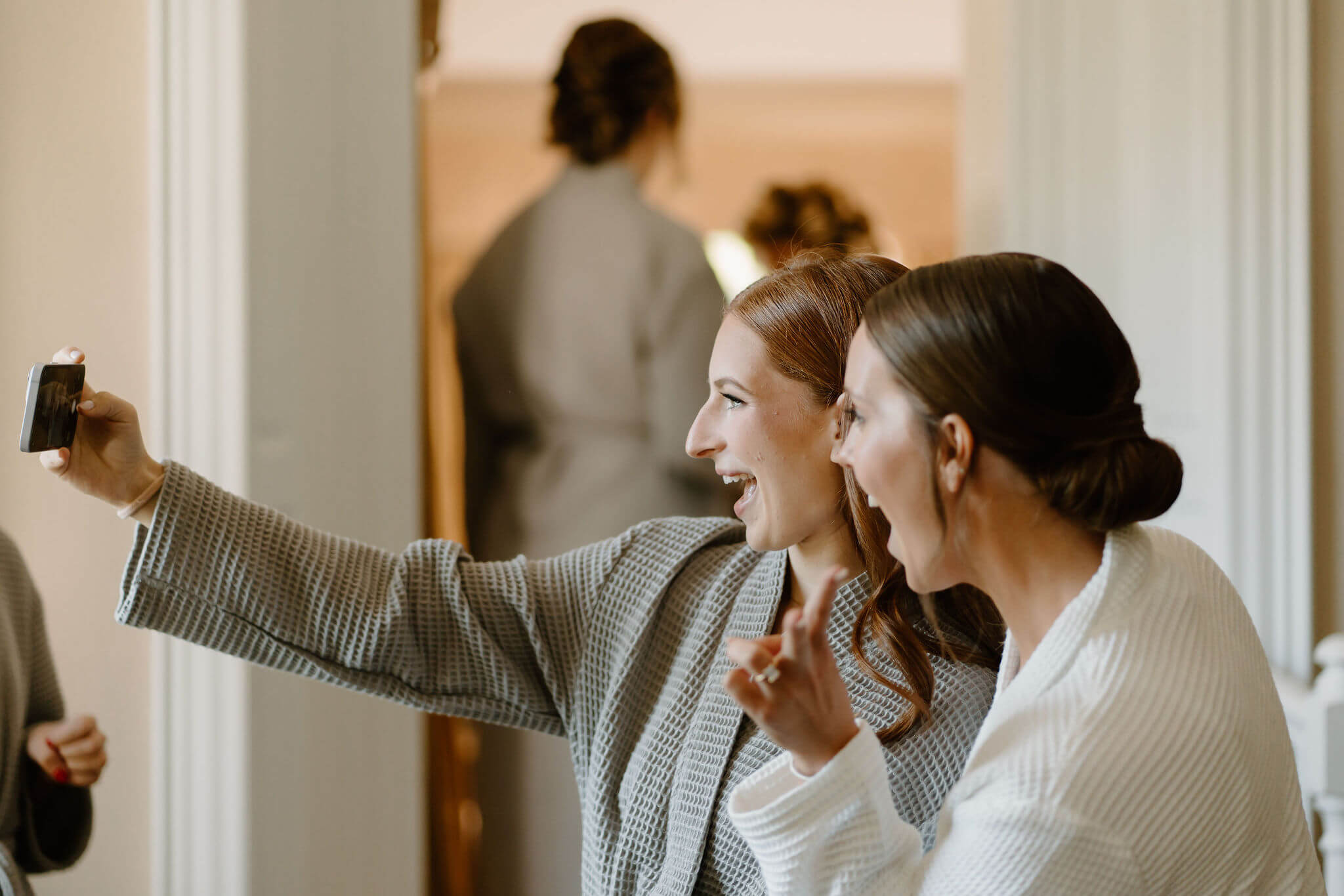 bride (white robe) and bridesmaid (gray robe) taking a selfie