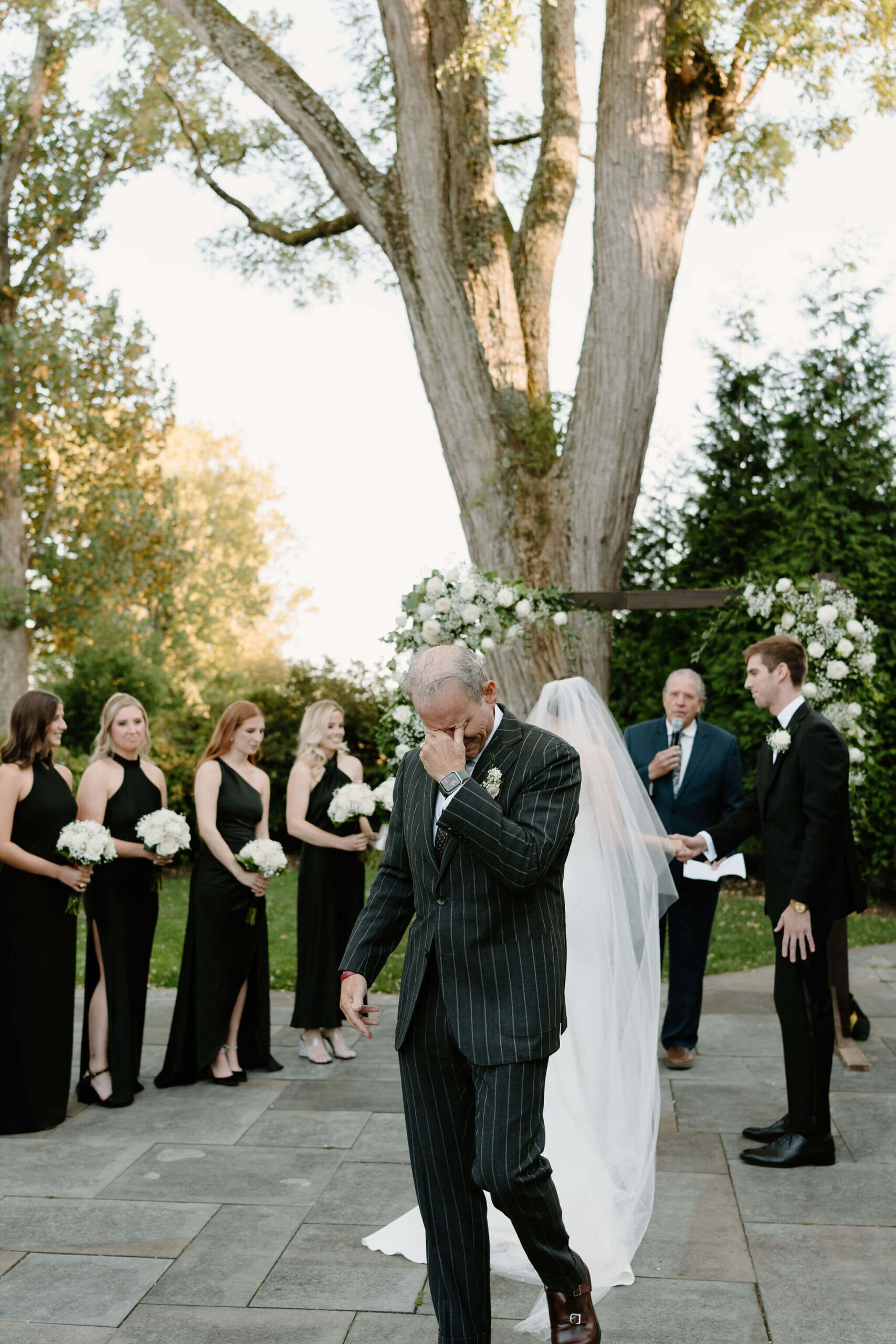 Father of the bride crying into his hand as he leaves his daughter at the wedding altar