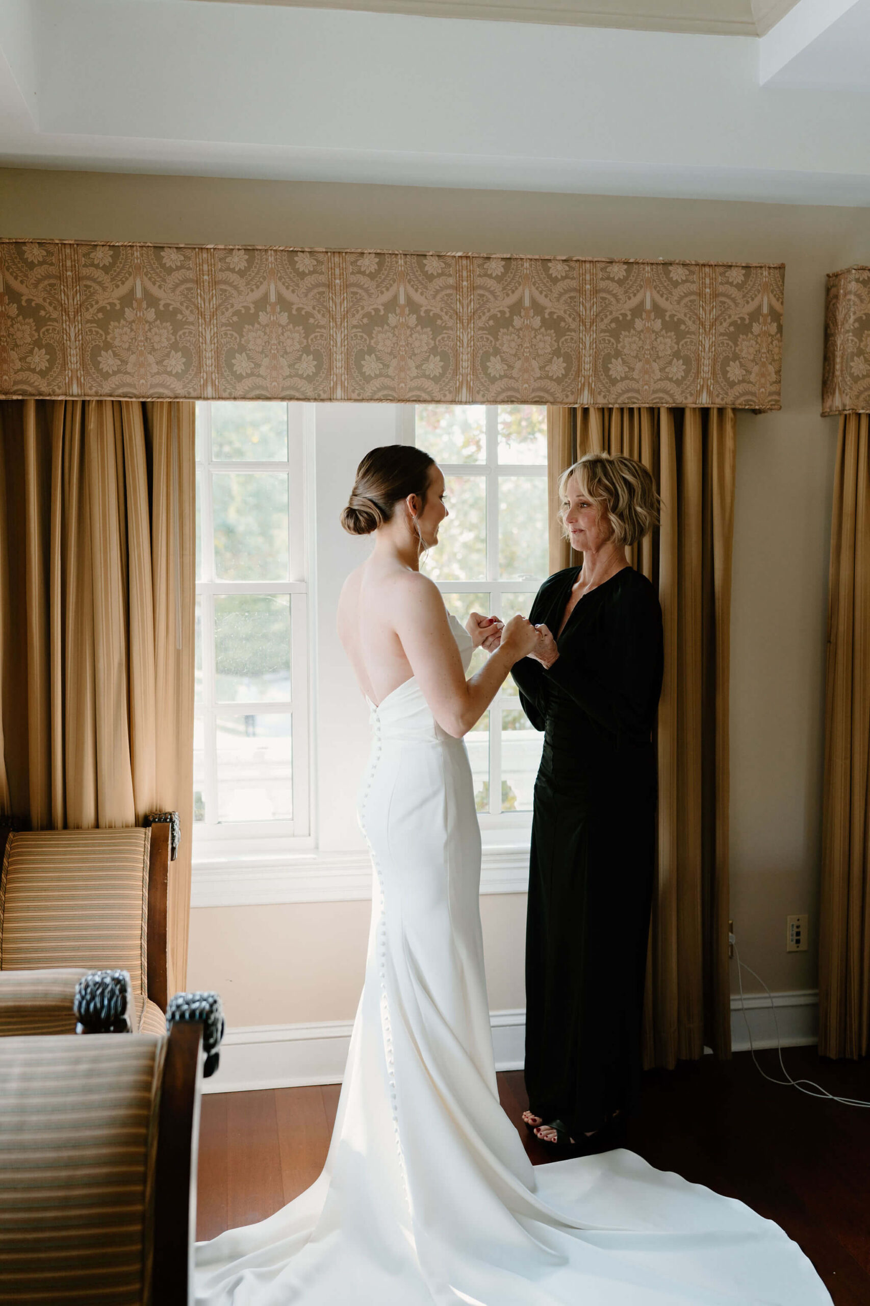 bride and her mother holding hands and smiling at each other