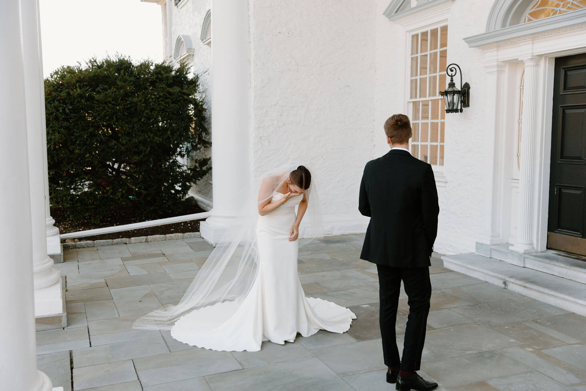 bride bent over with her hand to her face crying as her groom turns around during their first look