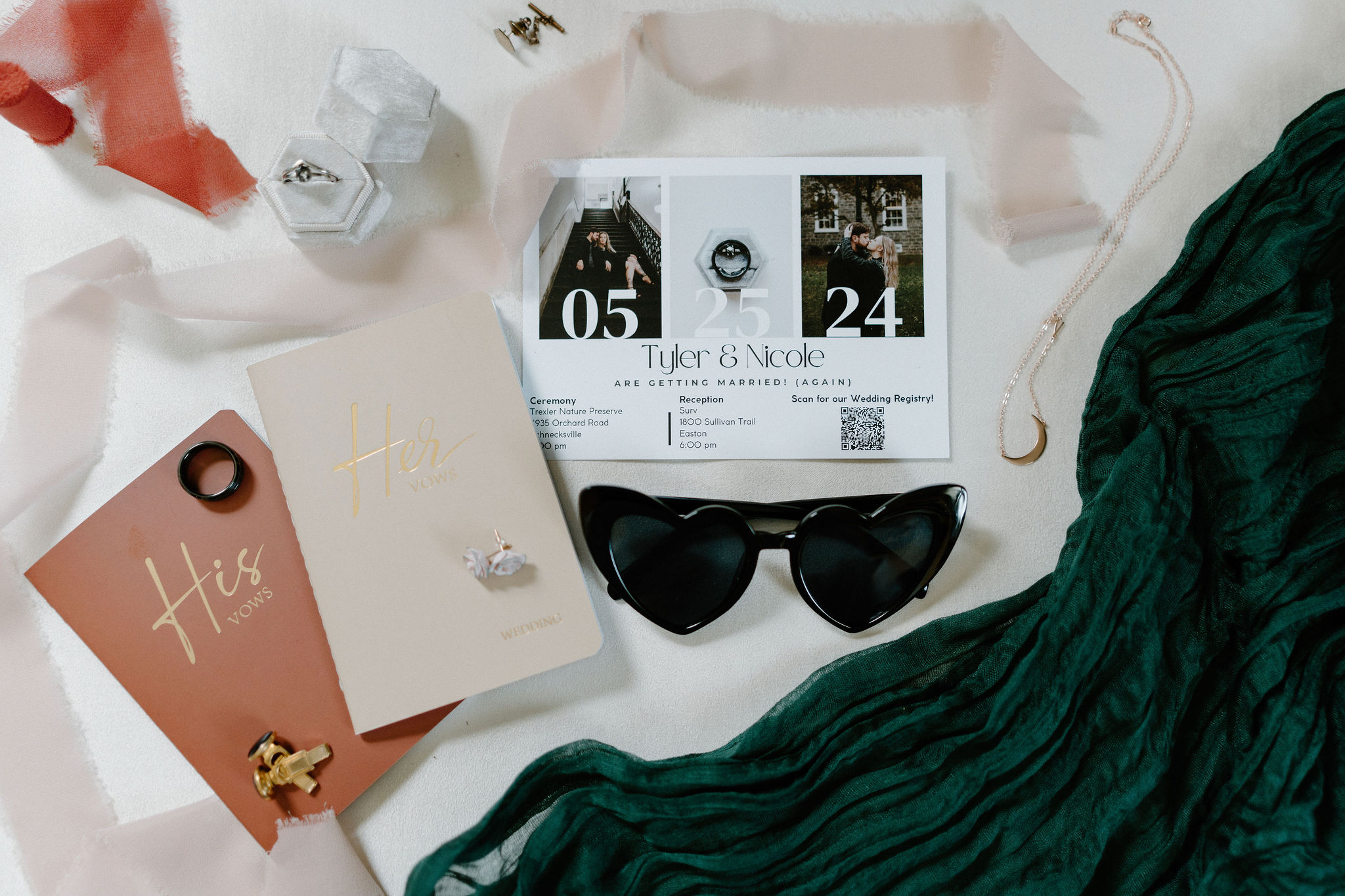 wedding details flat lay including his and her vow books, cuff links, wedding bands, and engagement ring, heart shaped sunglasses, an invitation suite, jewelry, and ribbons