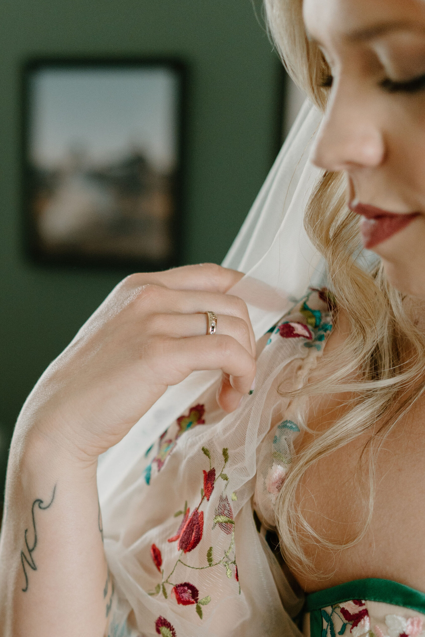 close up of a bride looking over her shoulder, focused on a ring on her right hand as she plays with her veil.