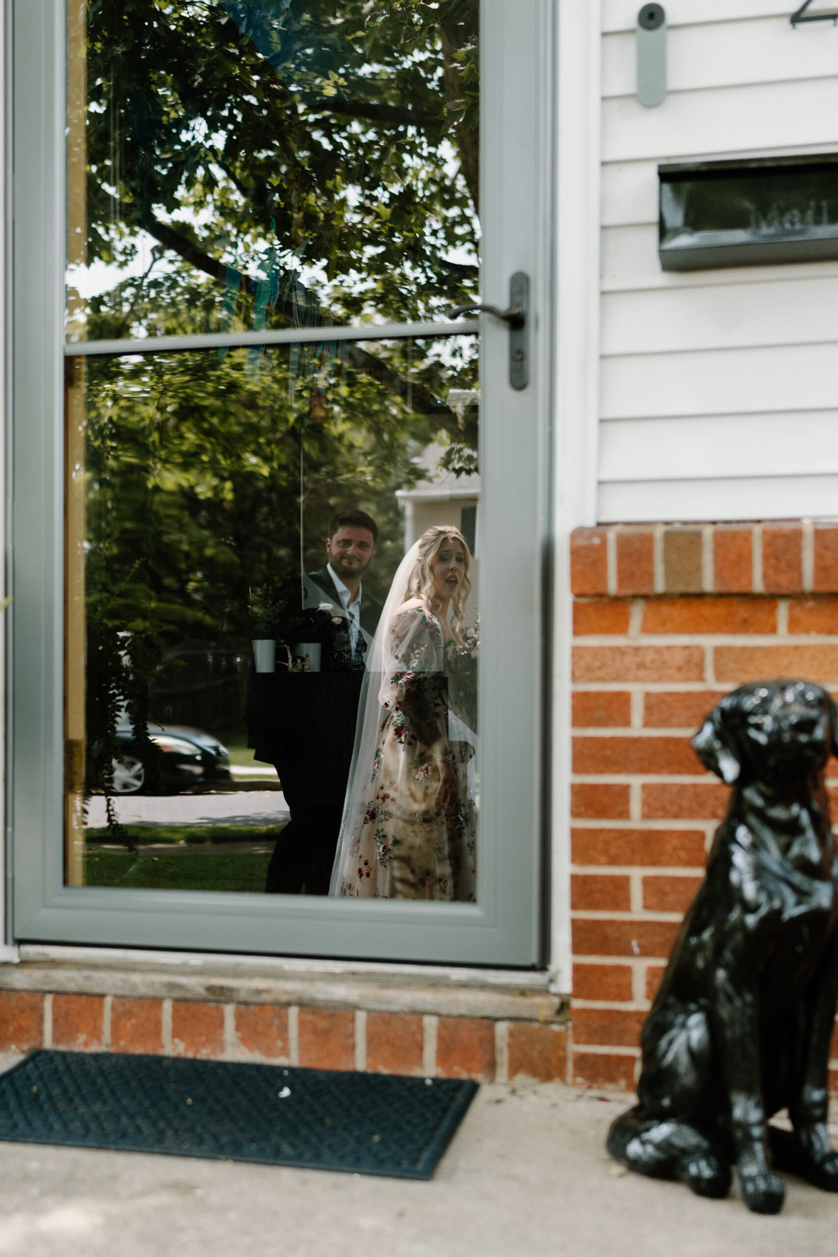 the bride and groom's cat looking at them through the glass storm door, with the reflection of the bride and groom smiling back at the cat