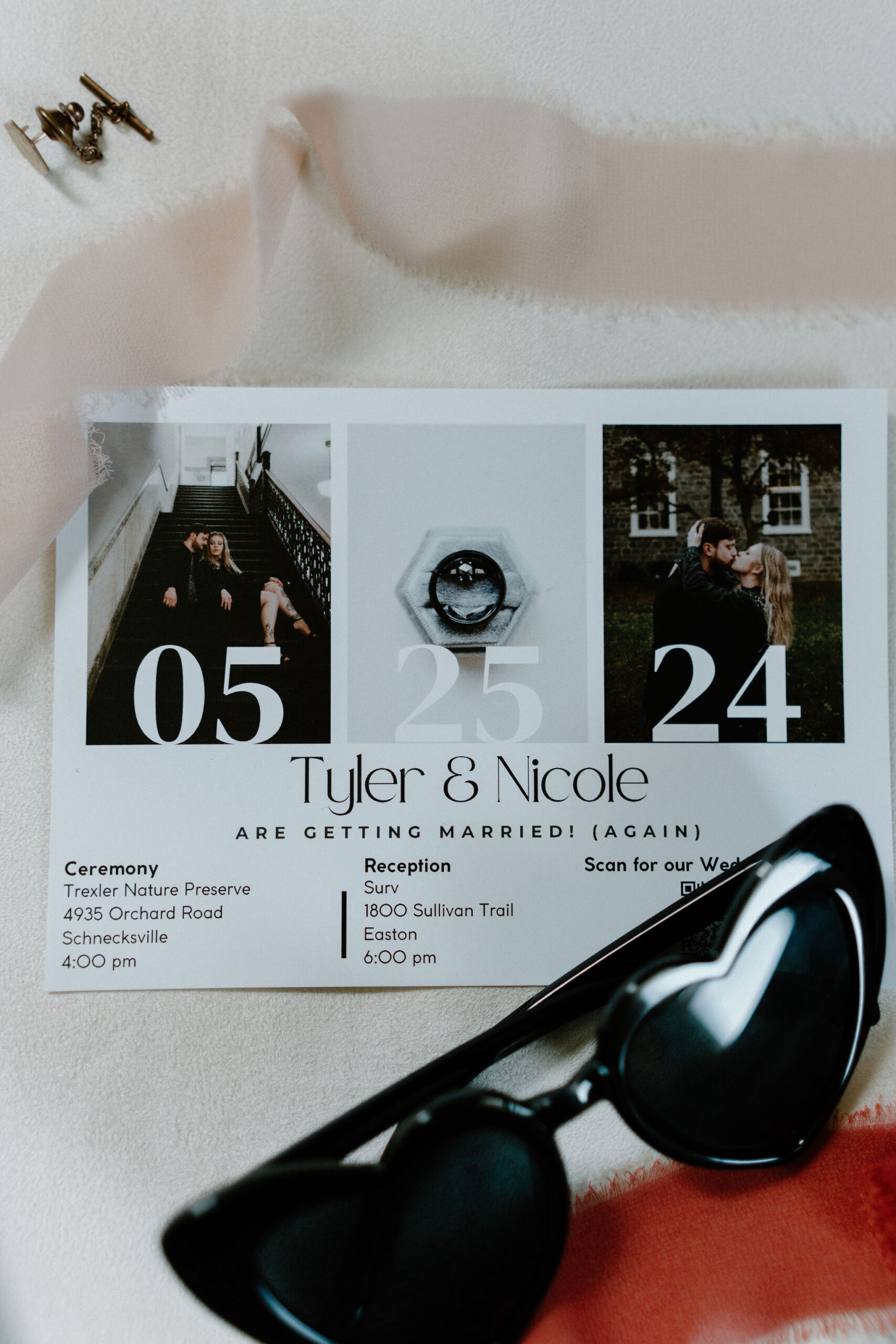 wedding details flat lay kit including an invitation suite, black heart shaped glasses, and a pin