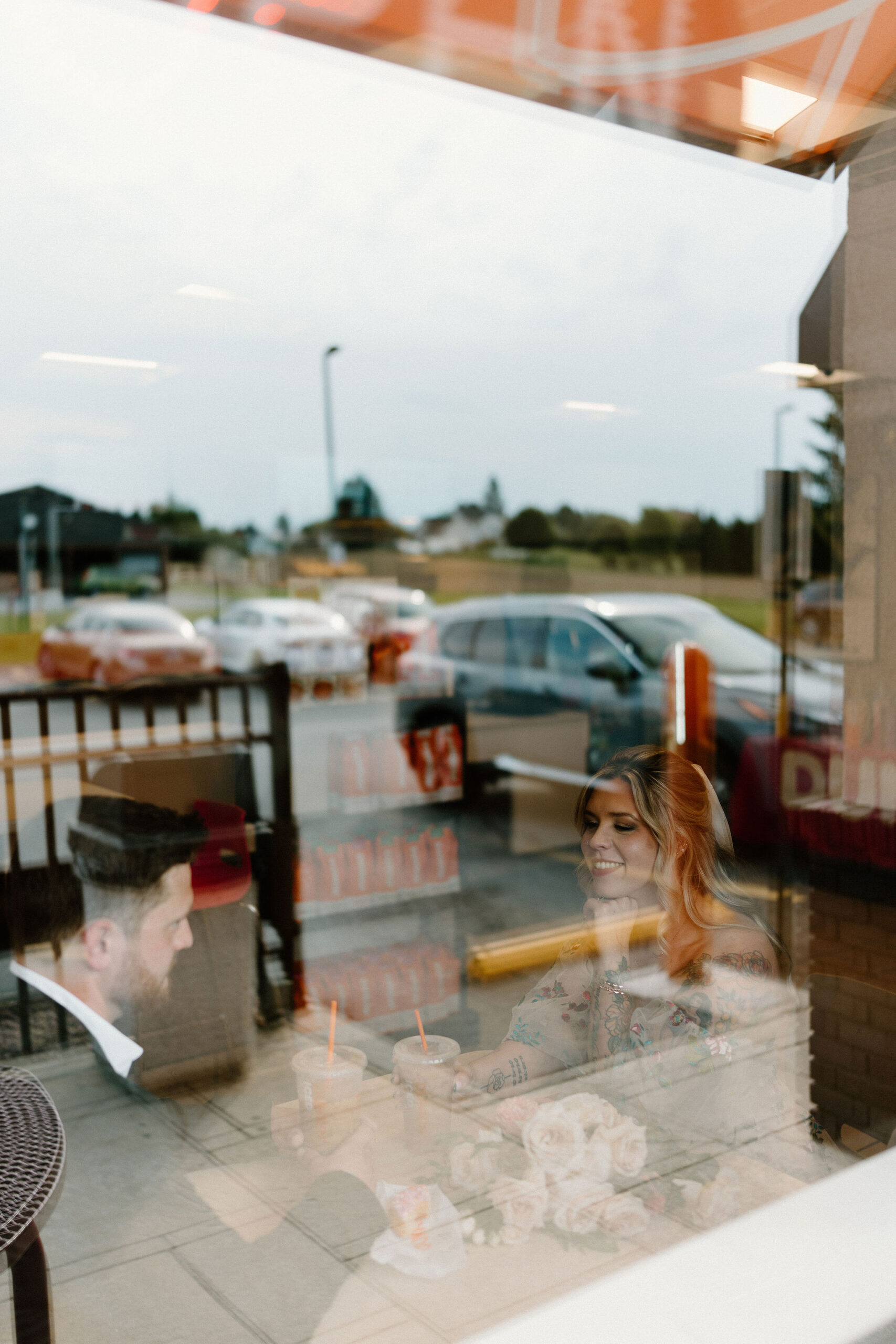 bride and groom sitting across from each other at a table in a Dunkin Donuts, photographed through an exterior window
