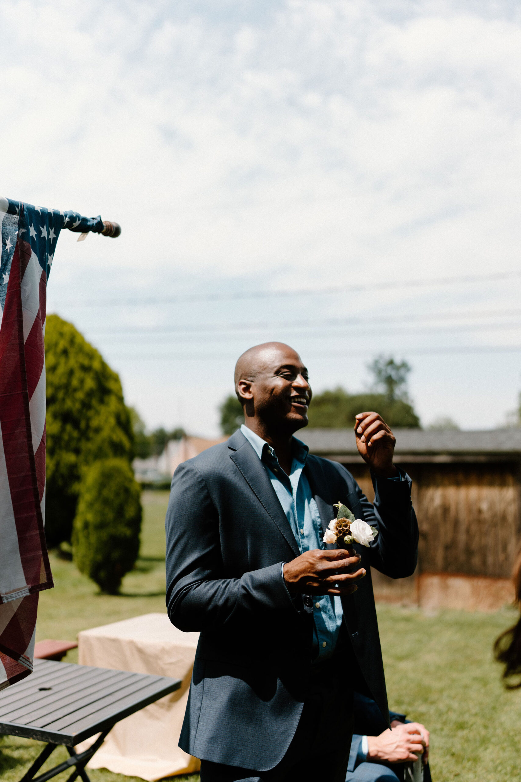 groomsman standing in the sun, holding a boutonniere and laughing