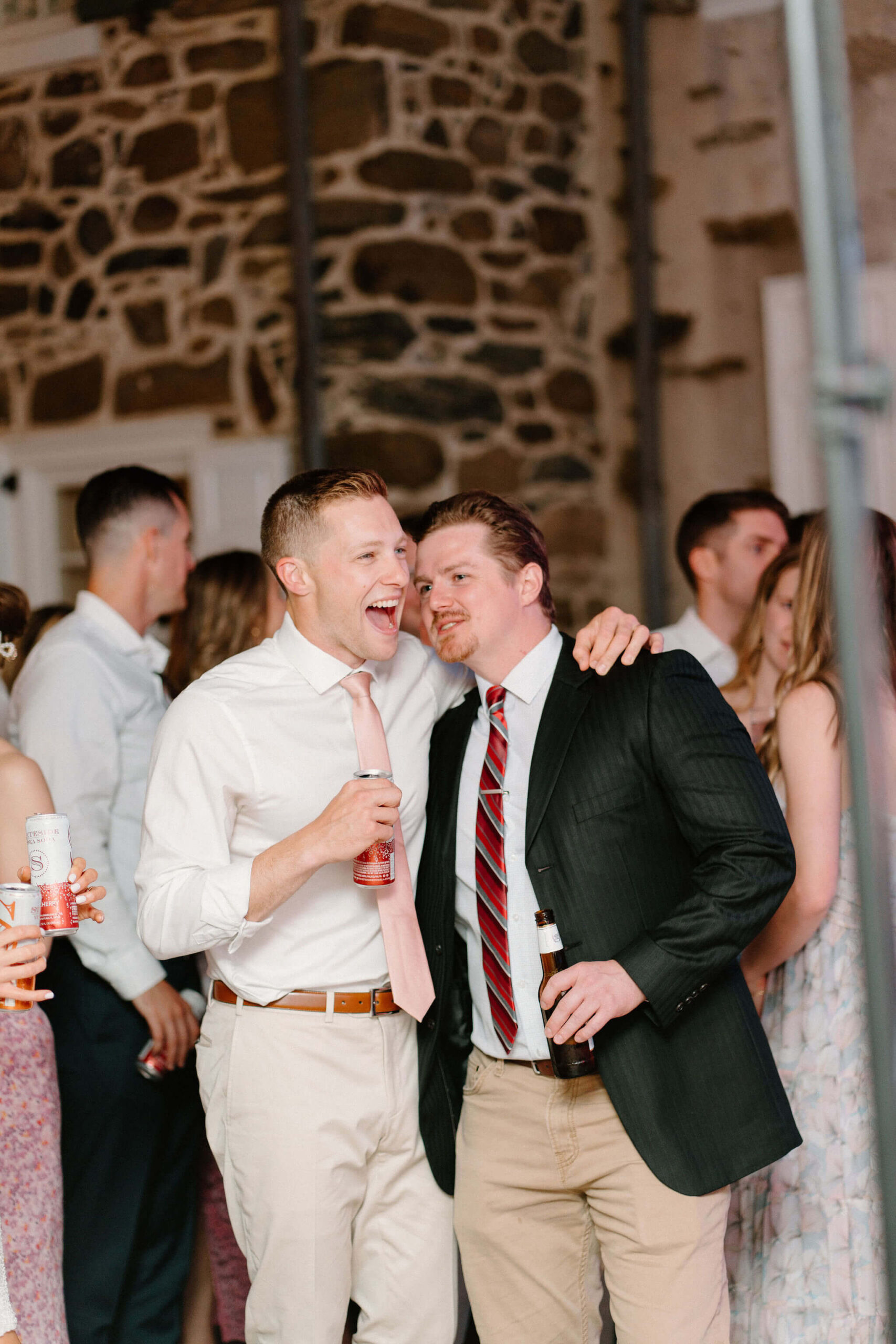 groom laughing with his arm around a friend on the dance floor at his wedding