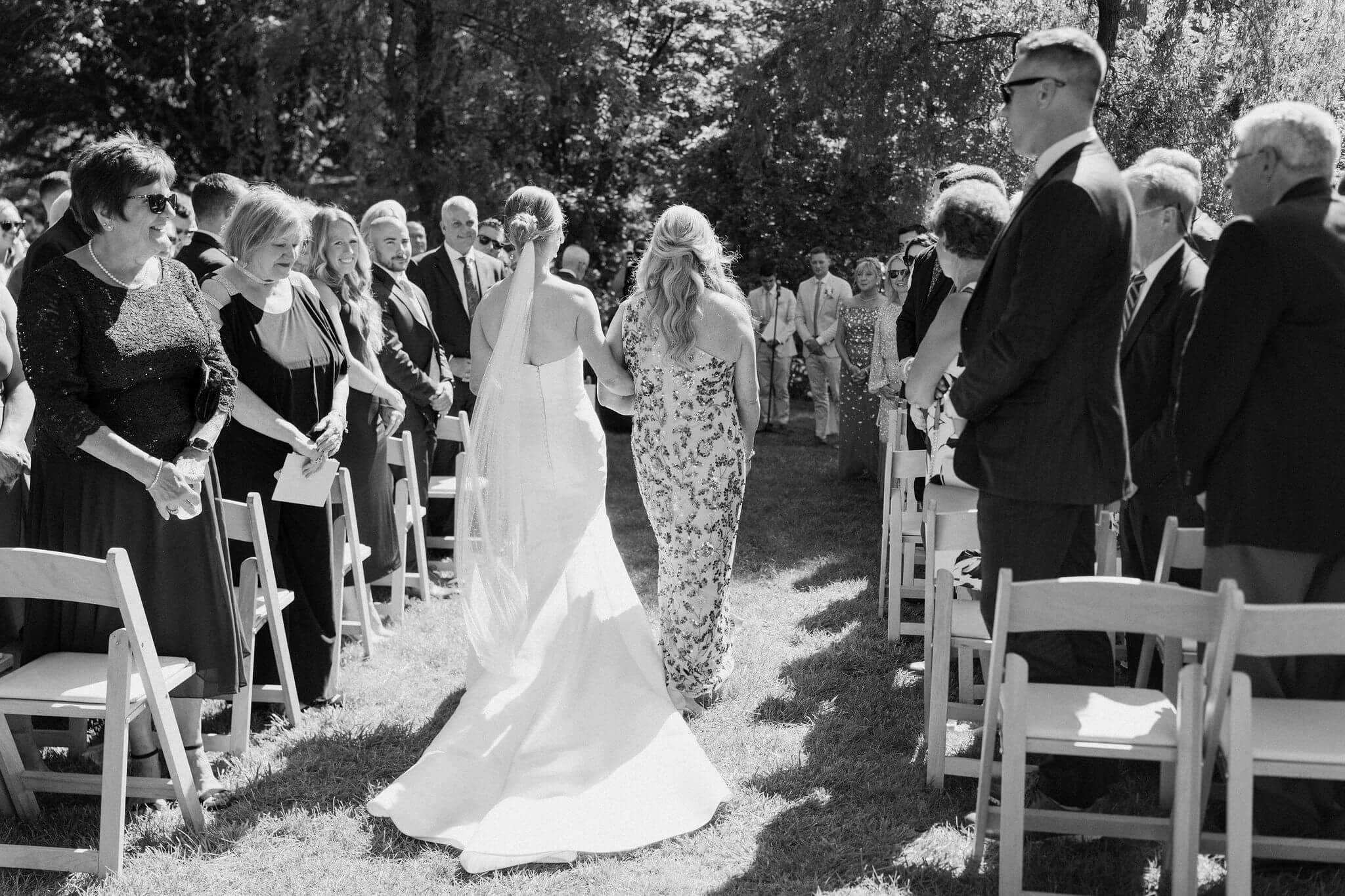 black and white image of bride being walked down the aisle of her wedding ceremony by her mother