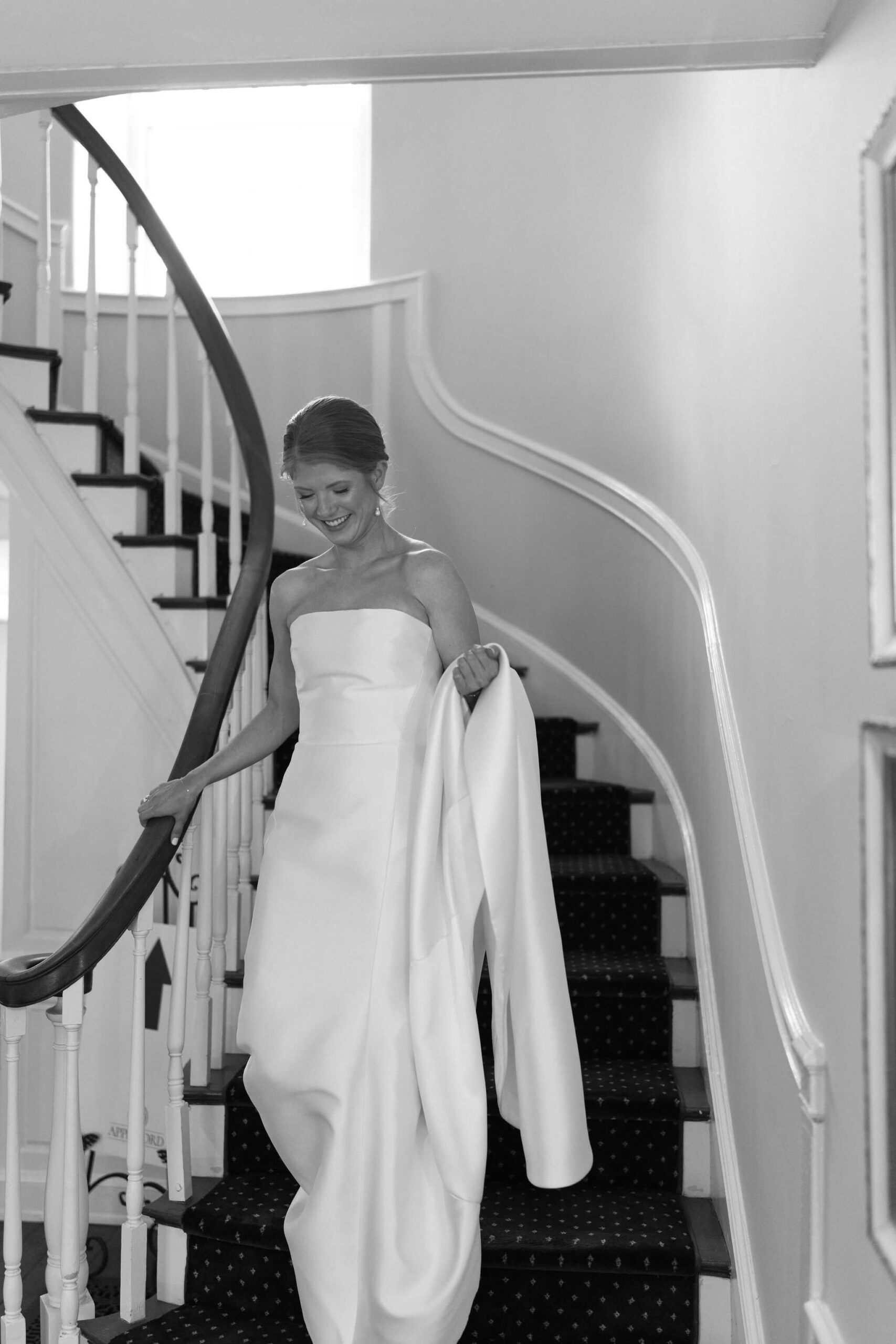 black and white image of bride walking down the stairs, holding her train