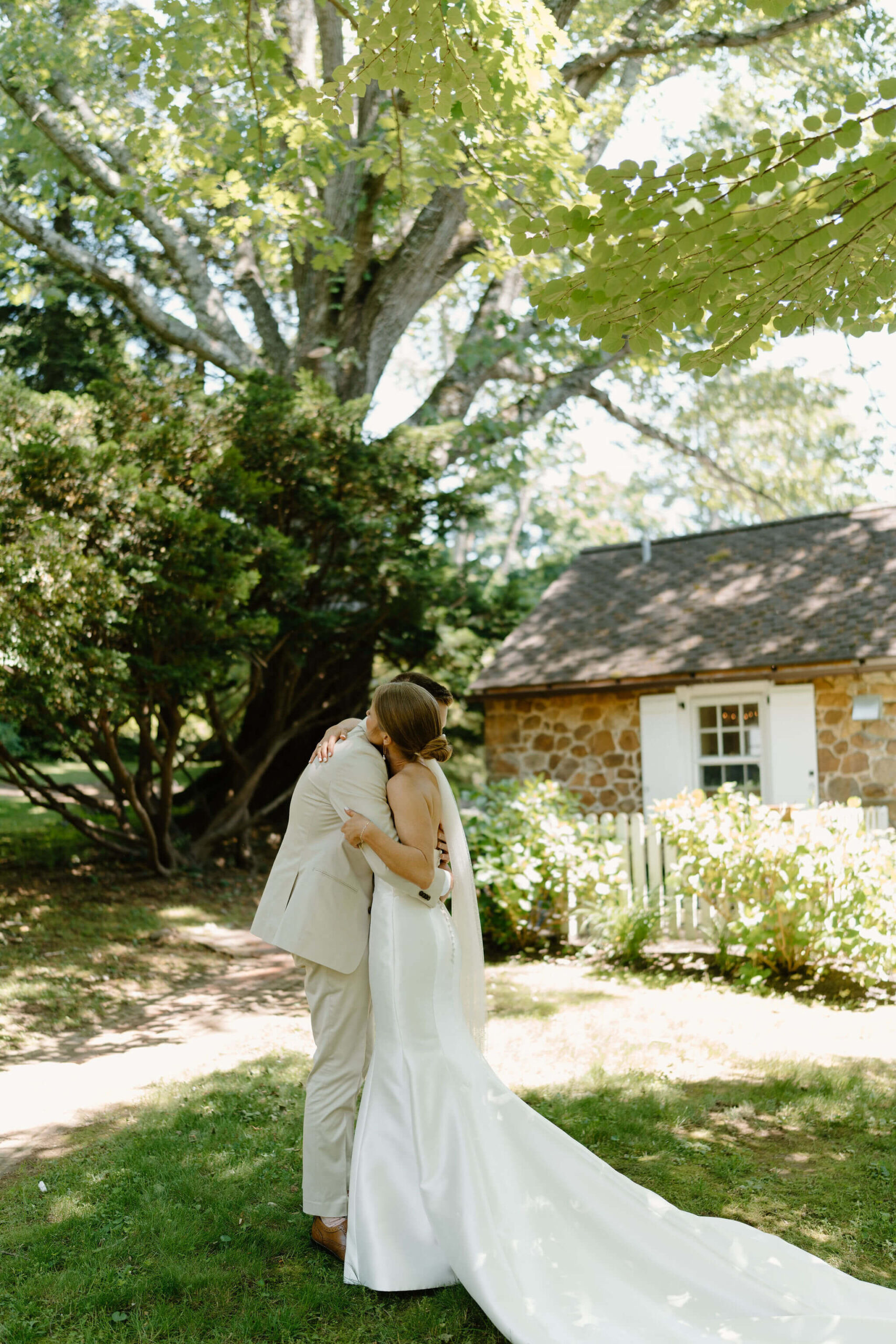 bride and groom embracing during their first look, against a stone building with trees behind them