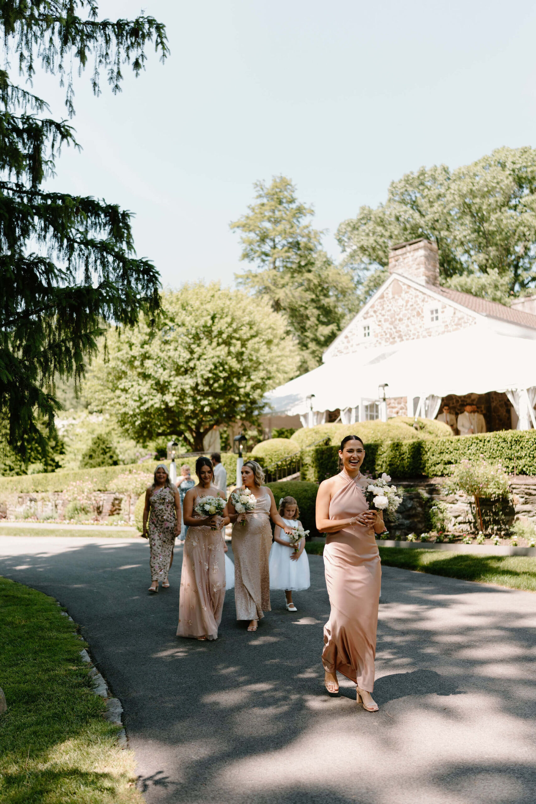 bridesmaids and flower girls smiling and walking down a paved road, wearing mismatched pink dresses