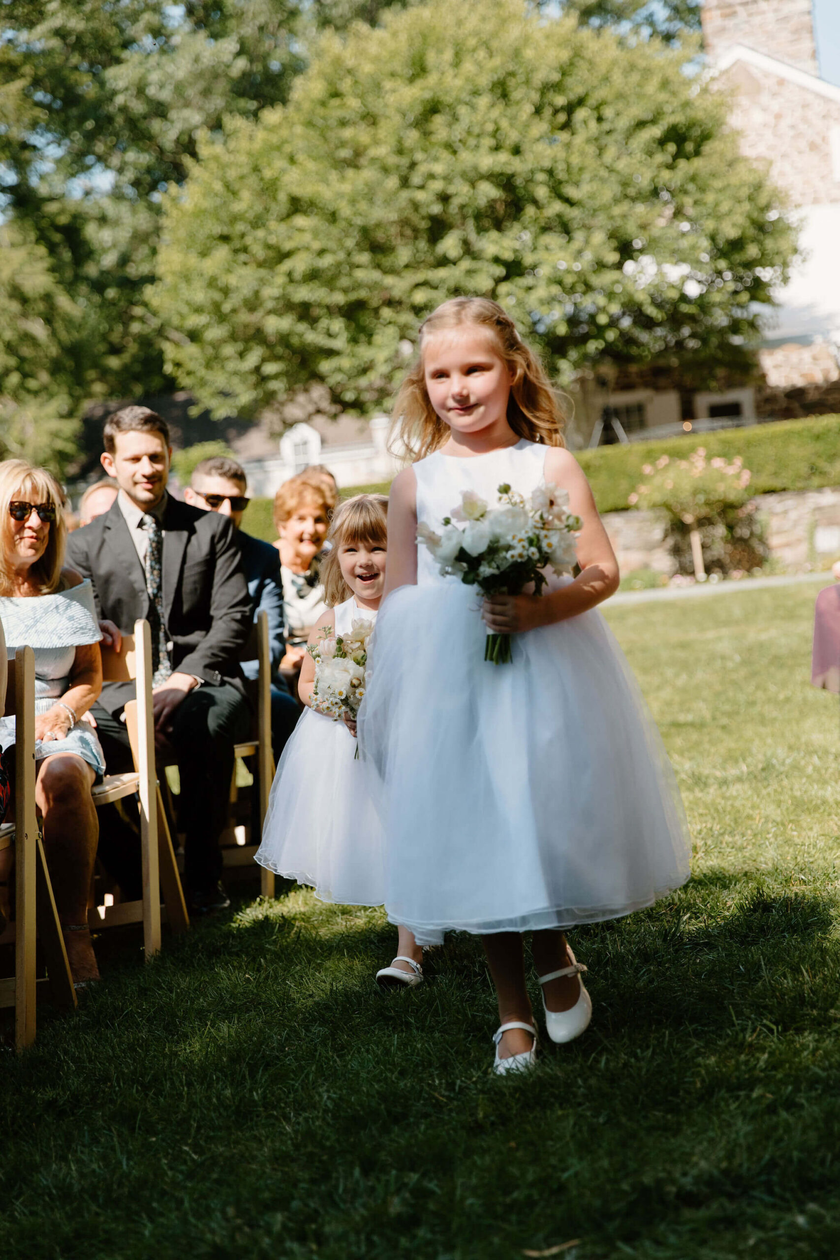 flower girls wearing white dresses, holding bouquets and walking down the aisle