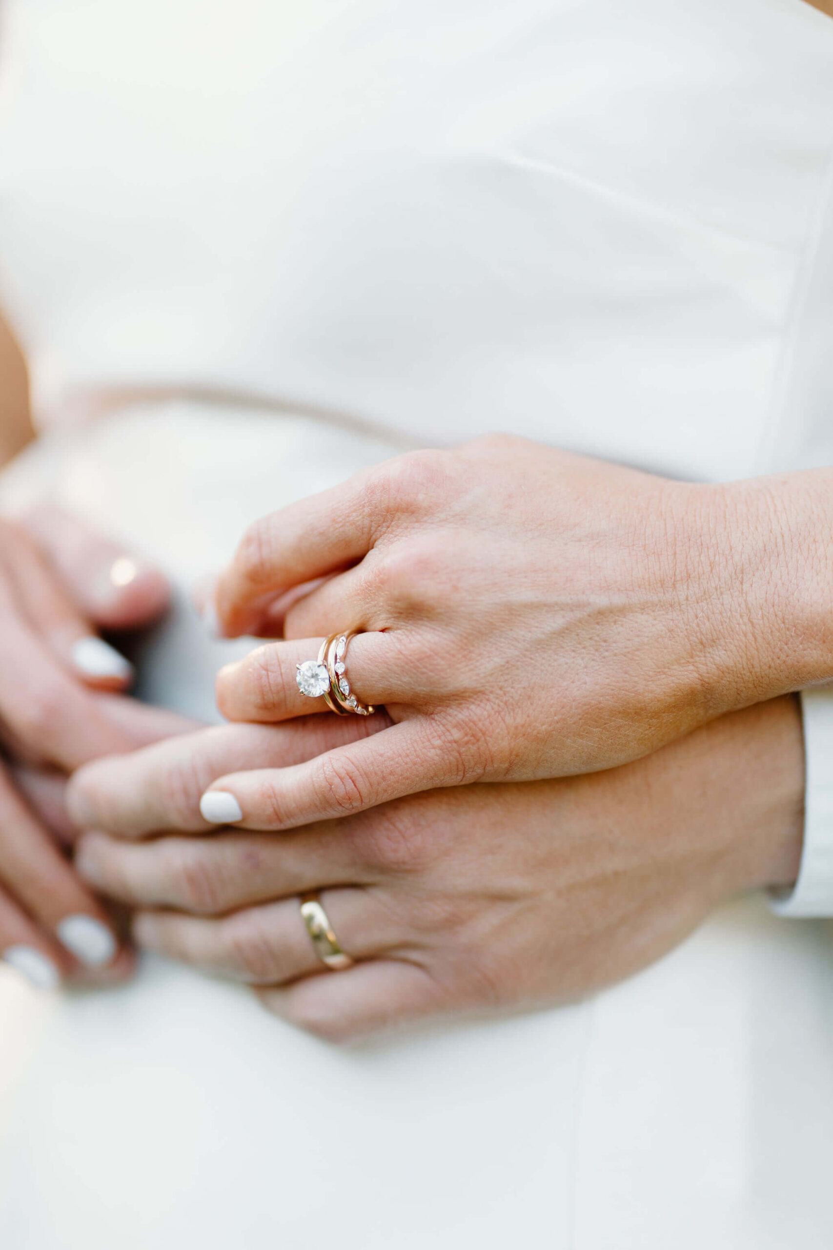 close up of bride and groom's left hands over each other, focused on her engagement ring and their wedding bands