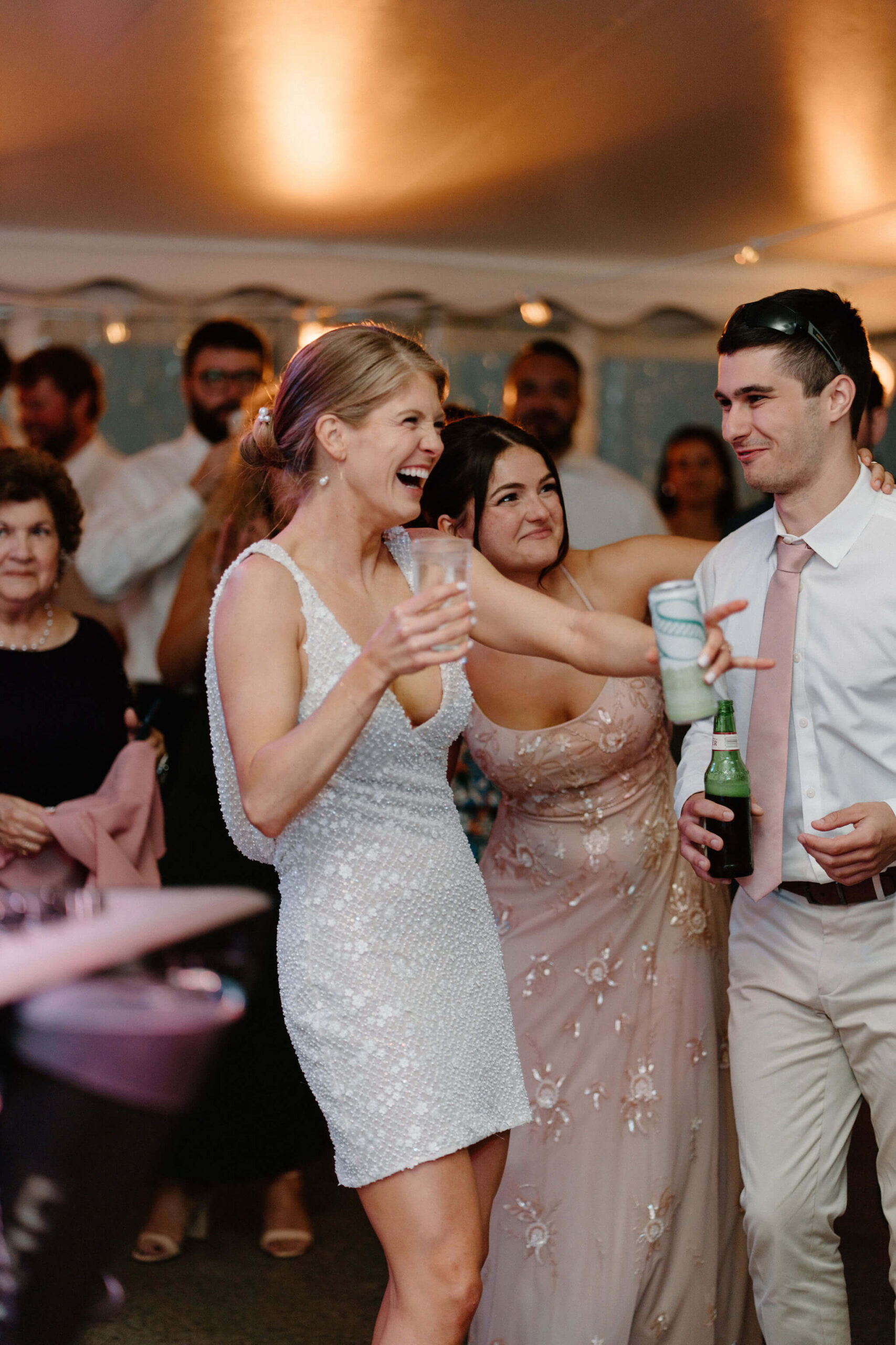 bride in a short, v-neck sequined dress laughing with her siblings at her wedding reception