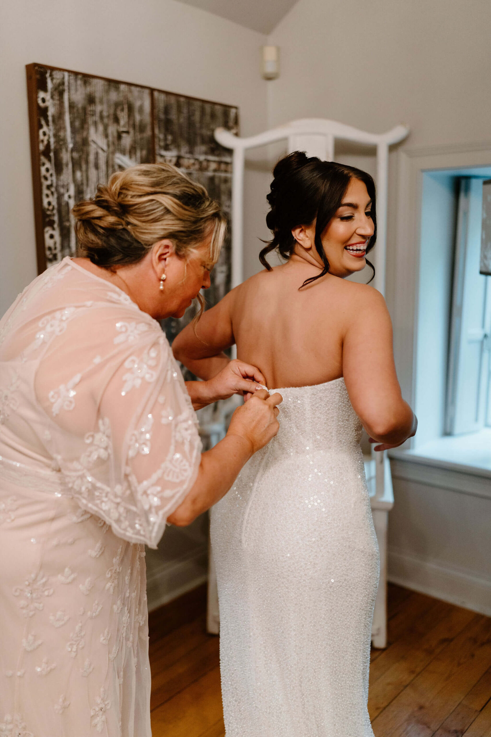 bride's mother (pale pink dress) zipping bride into her sparkly wedding gown