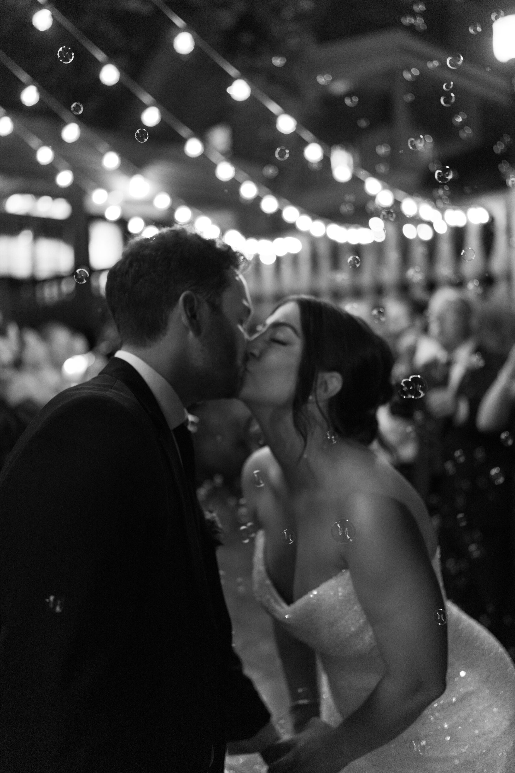 black and white image of bride and groom kissing, surrounded by bubbles