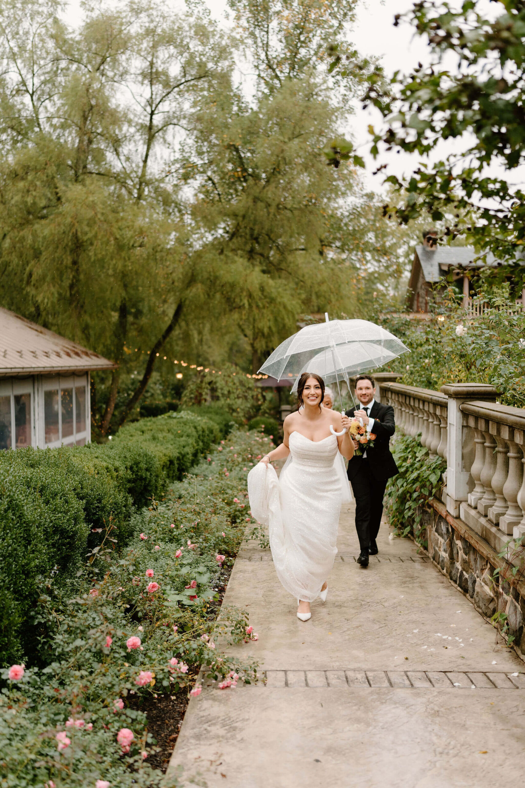 bride and groom walking up a path smiling with their umbrellas