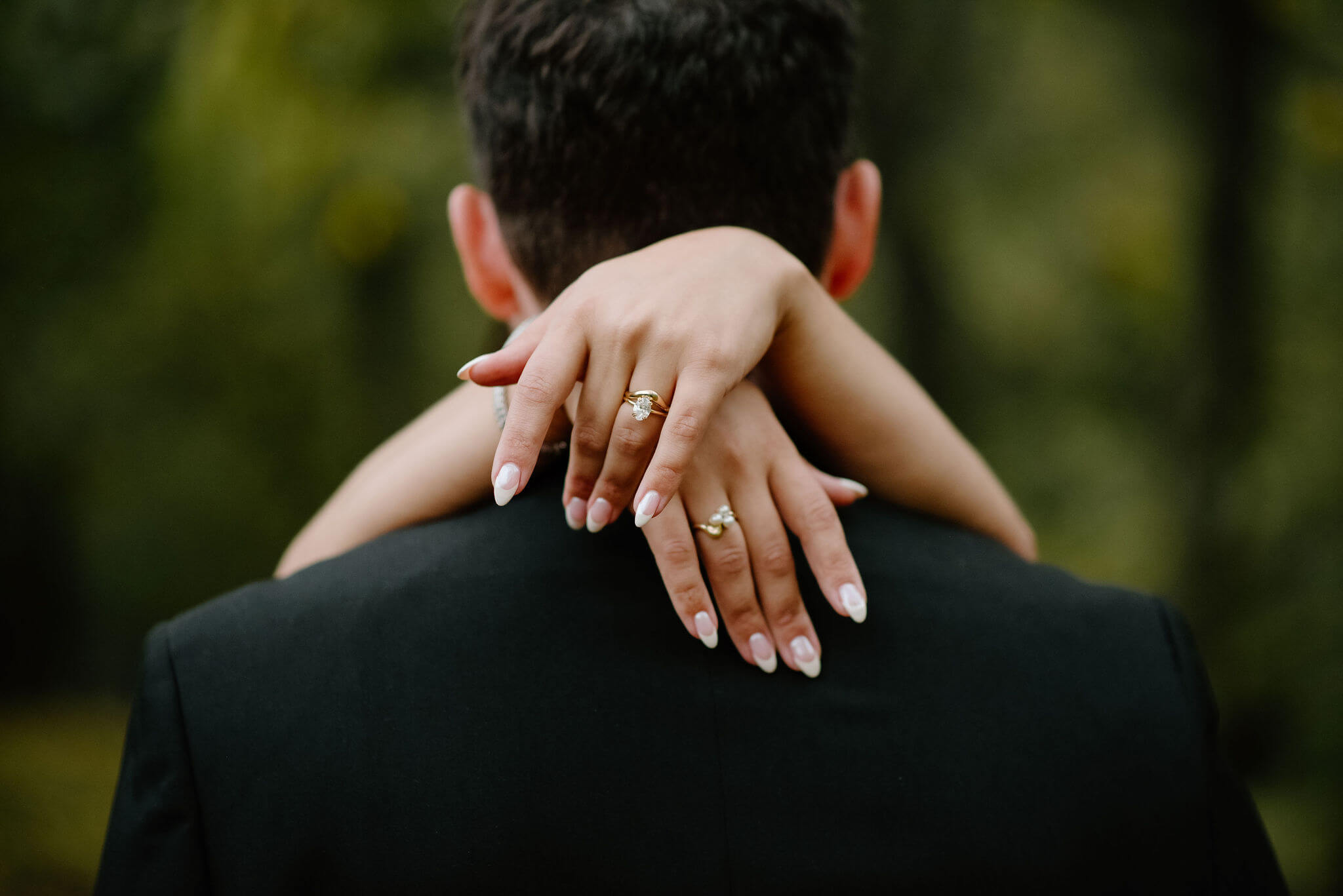 close up image of bride's hands, focused on her engagement ring and wedding band, thrown over the groom's shoulders