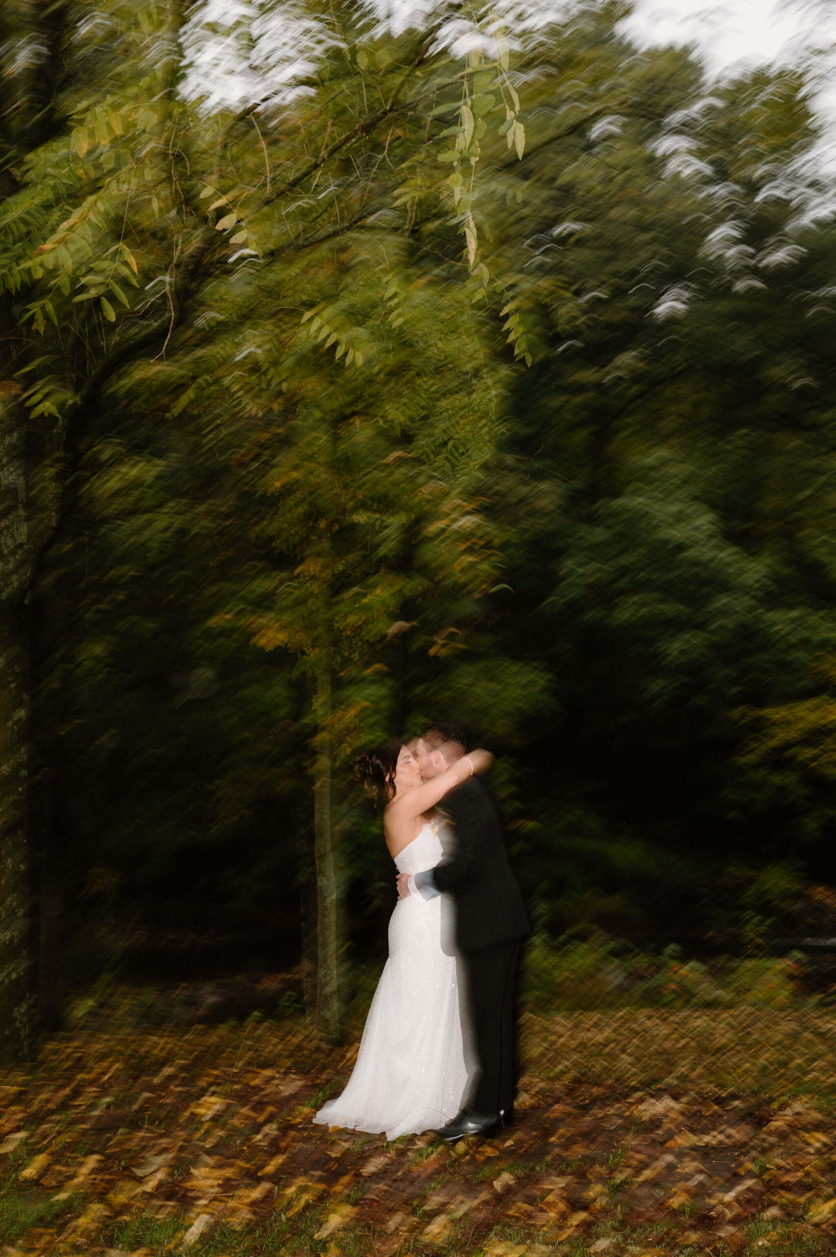 shutter drag image with a flash fired of bride and groom kissing in a woodsy setting at dusk