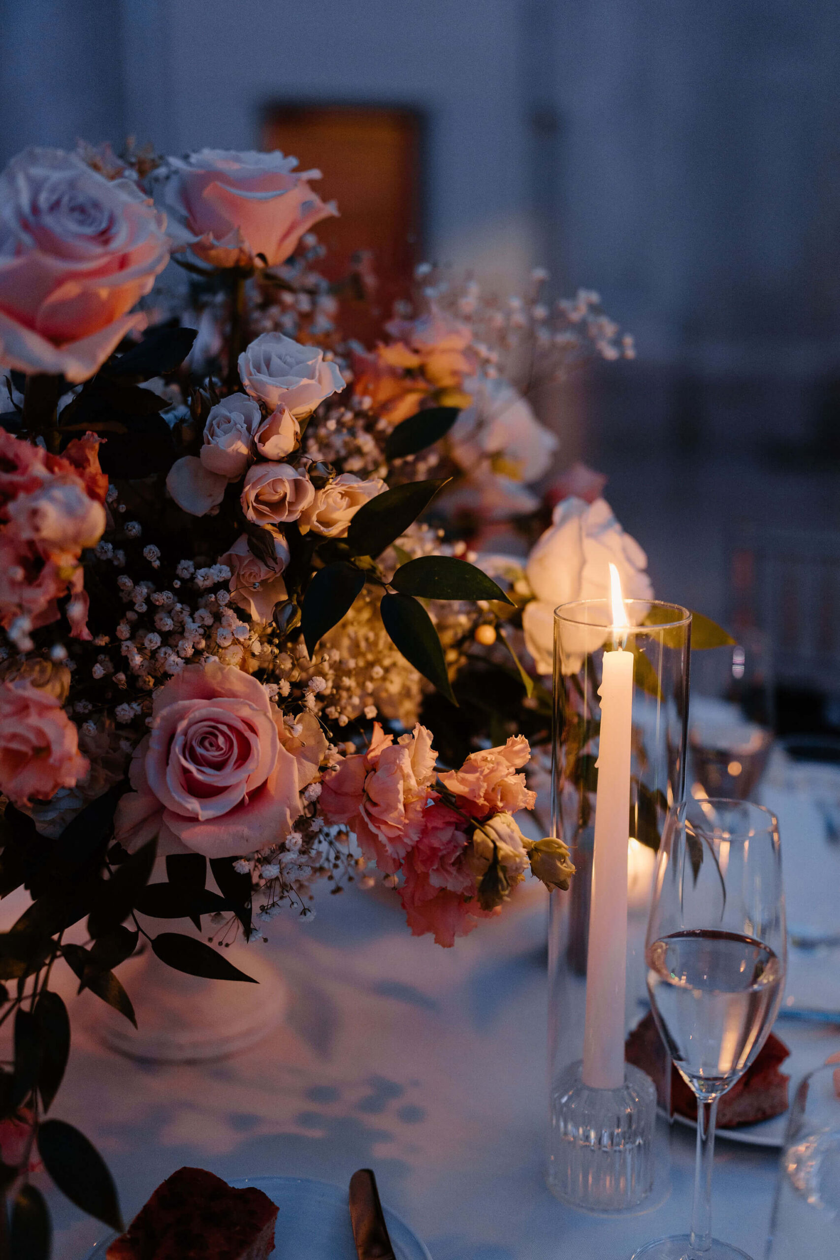 close-up of a pillar candle during a wedding reception, near a large floral display in the middle of the table