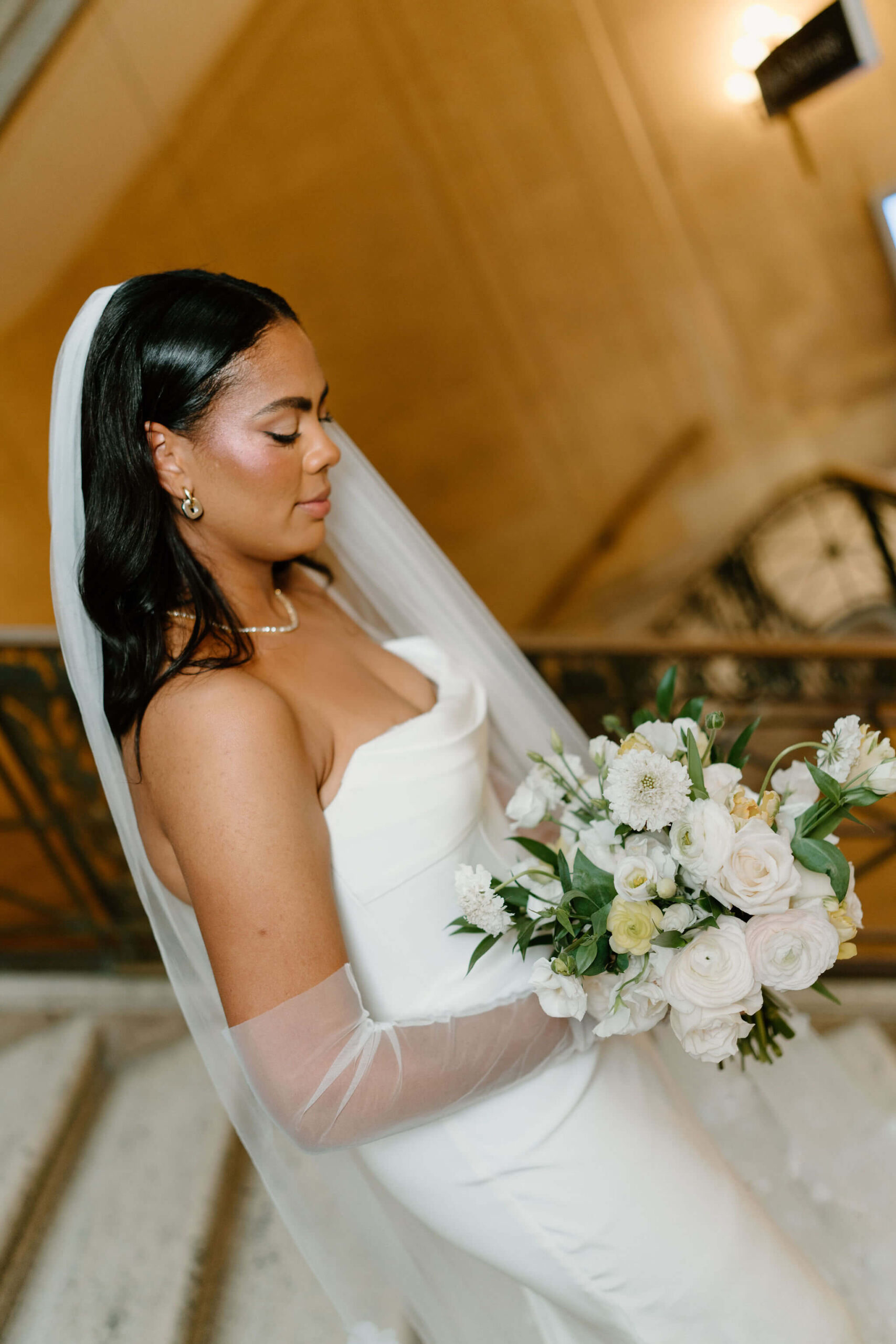 bride looking down at her bridal bouquet, standing in a wide marble staircase