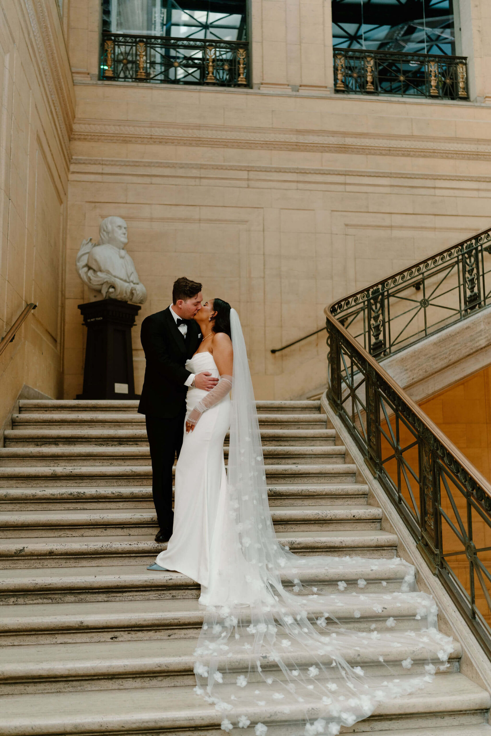 bride and groom kissing on large marble staircase, while bride's cathedral-length veil flows down the stairs behind her