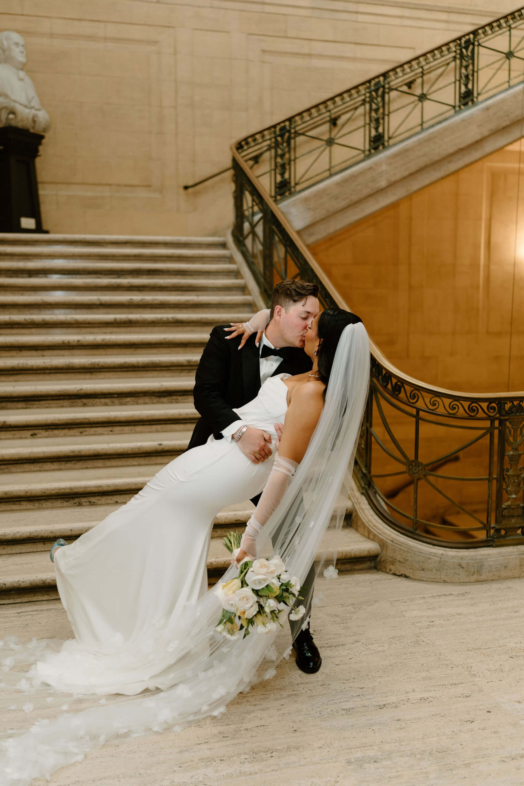 groom dipping bride in front of a wide spiral staircase at their franklin institute wedding