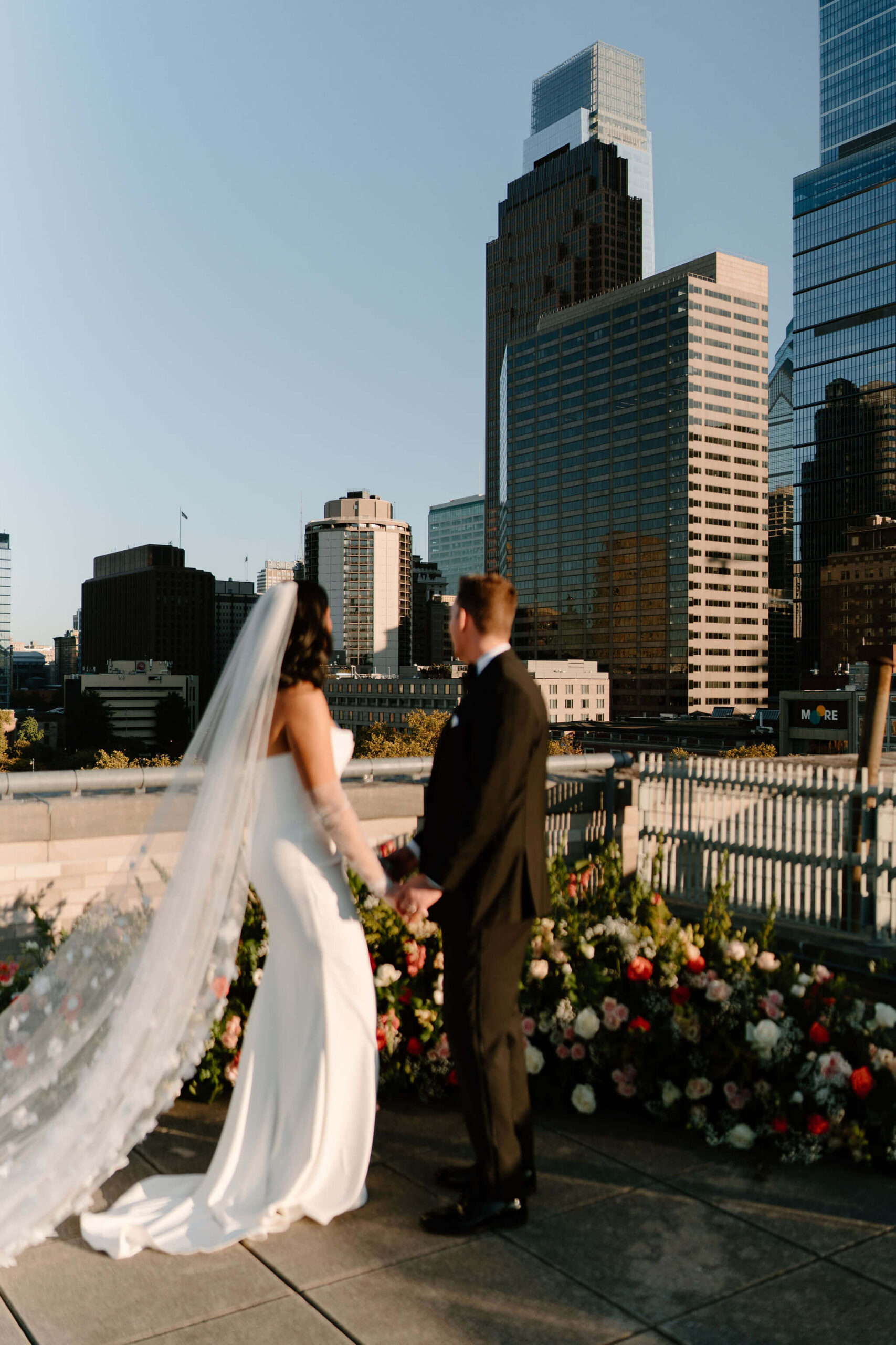 bride and groom holding hands on the roof and looking off at the skyscrapers in the distance at their franklin institute wedding