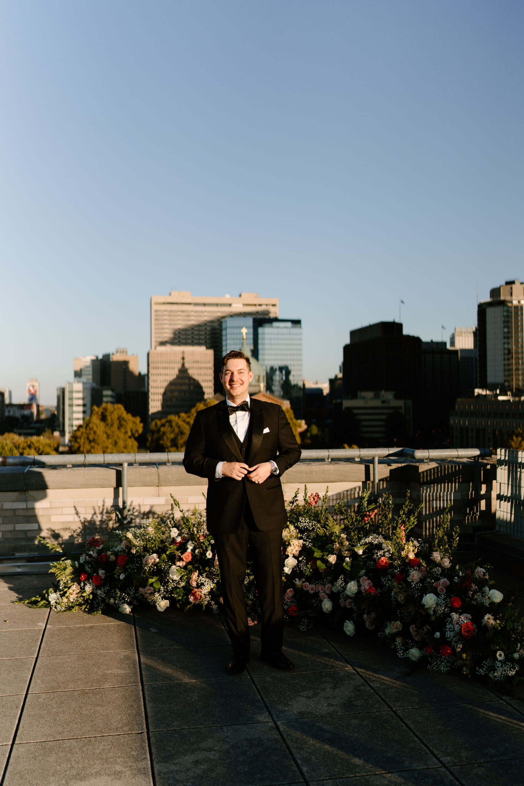groom standing in direct sun on the roof of the Franklin Institute, smiling into the camera with the Philadelphia skyline in the distance