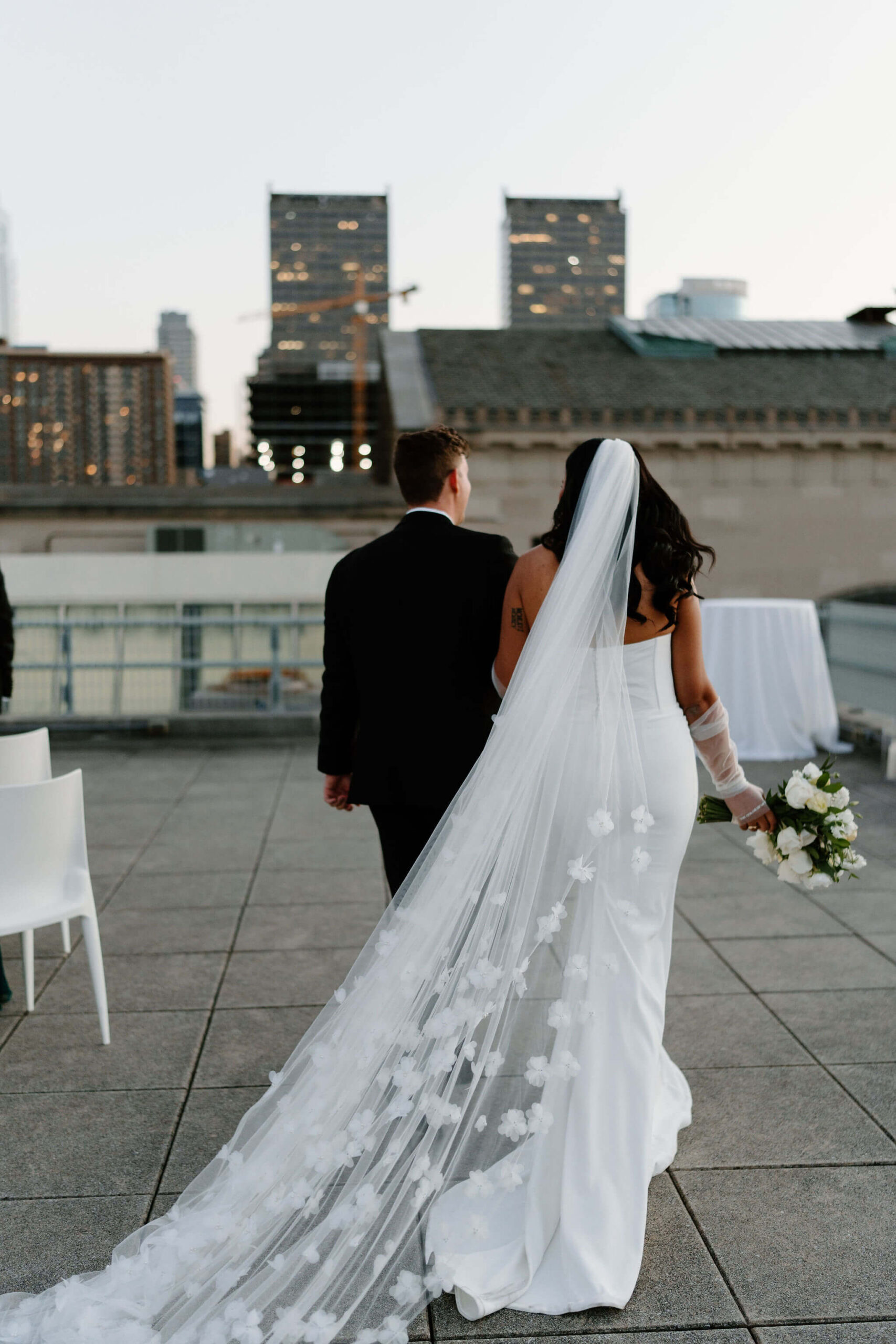bride and groom walking away from their rooftop franklin institute wedding ceremony, the train of the bride's veil trailing behind them